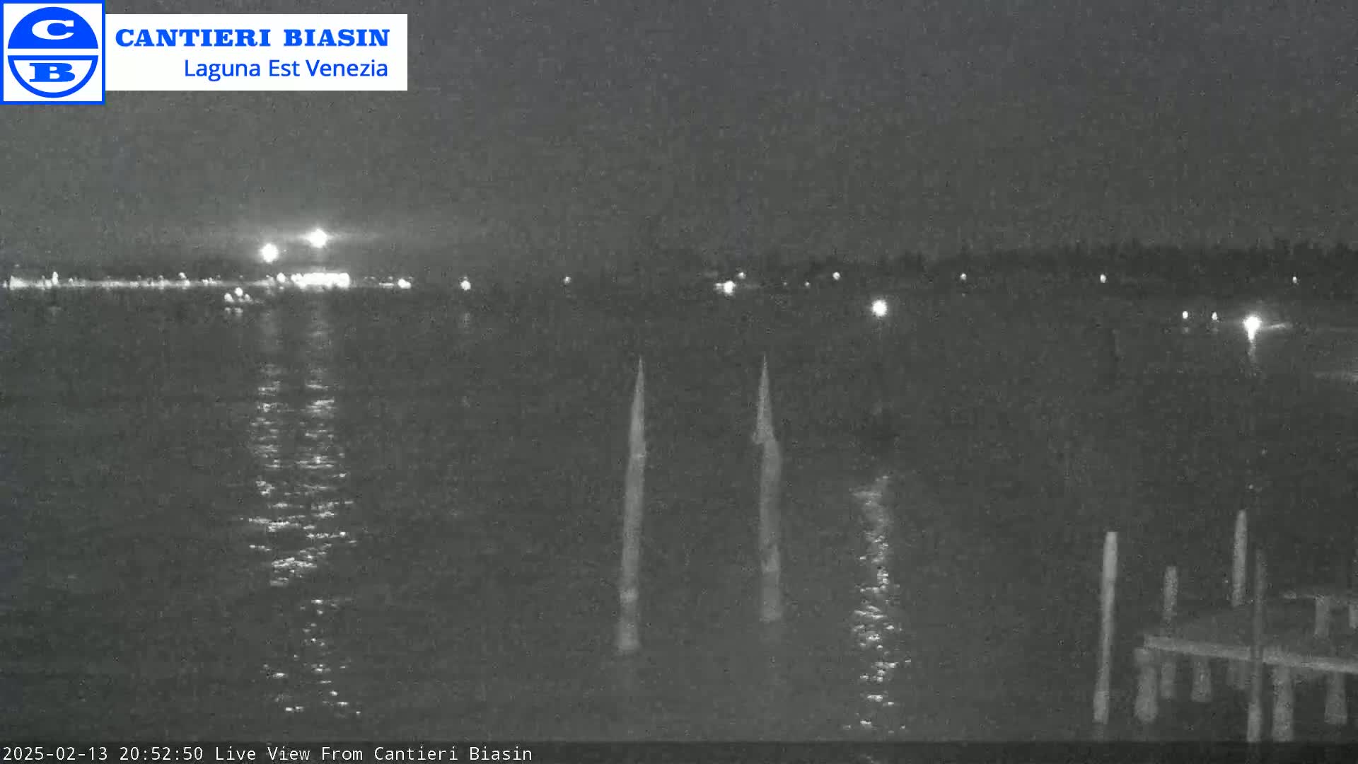 A nighttime view of a dark body of water with distant lights and two vertical posts in the foreground.