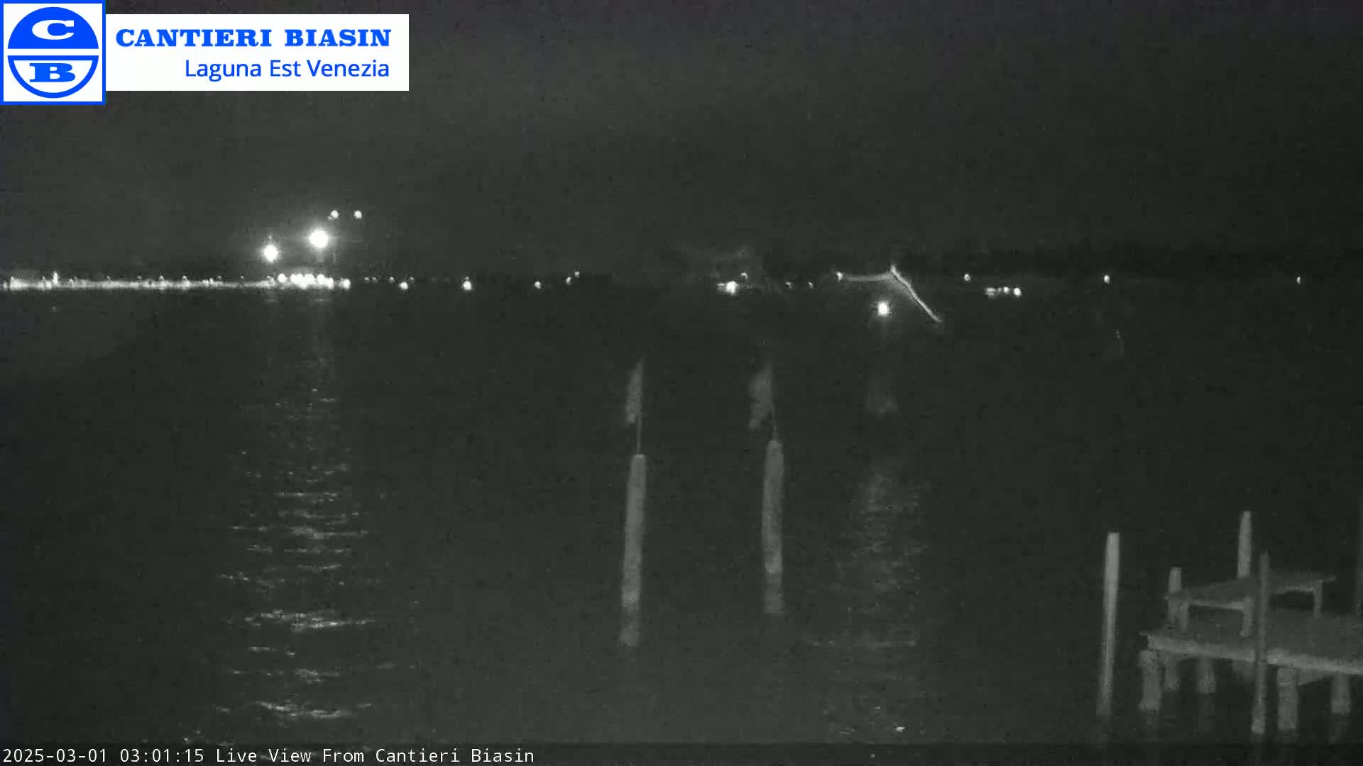 A nighttime view of a dark body of water with lights in the distance and a small dock in the foreground.