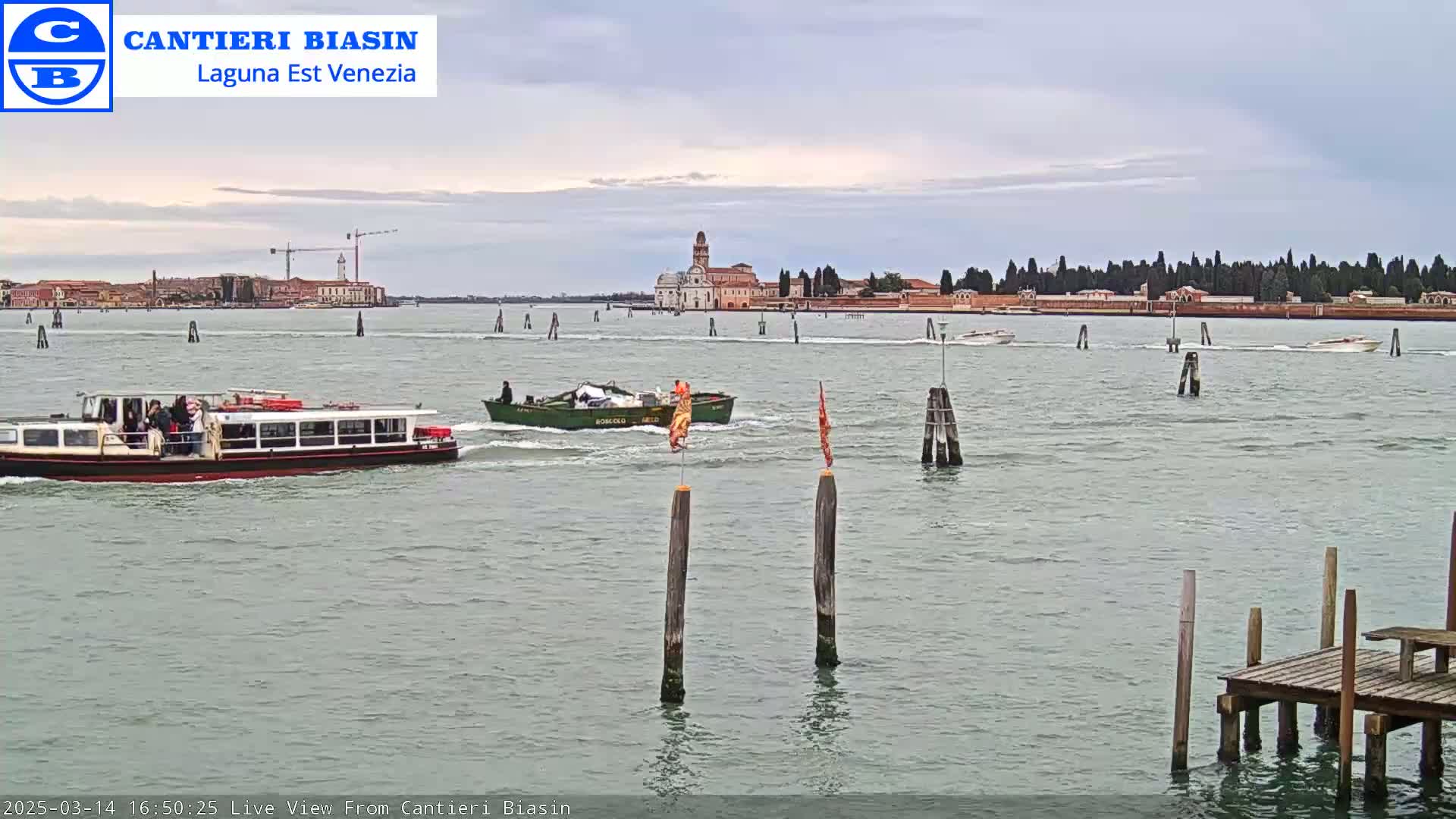 A calm, overcast day shows a waterway with several boats, including a passenger ferry, and a distant island with buildings.