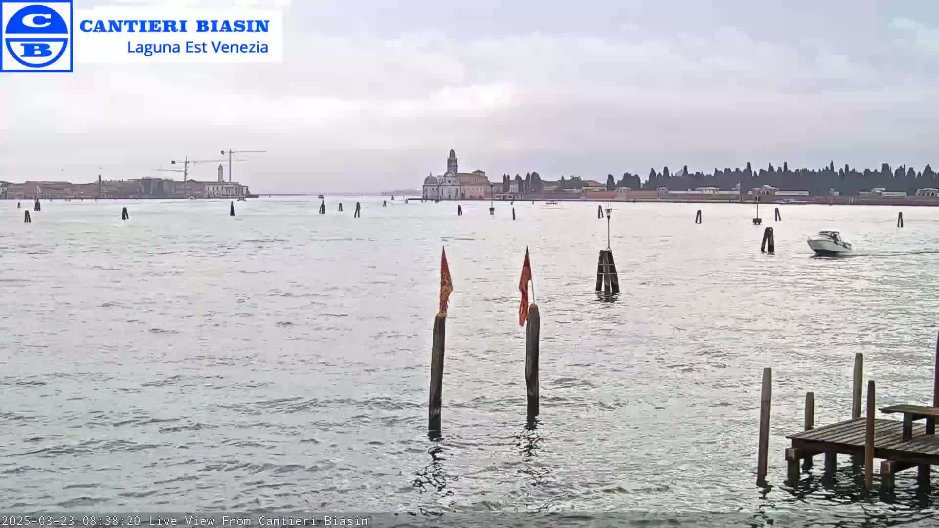 A body of water with a distant building and a small motorboat under an overcast sky.