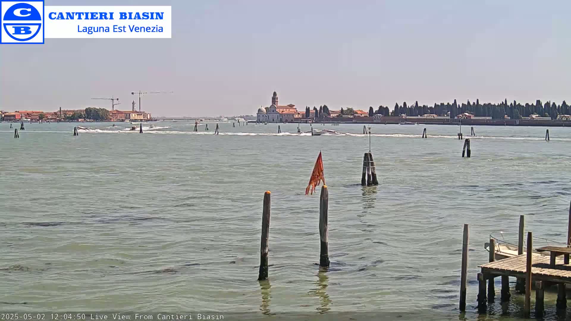 A calm, sunny day shows a body of water with several boats and a distant island featuring buildings and trees.
