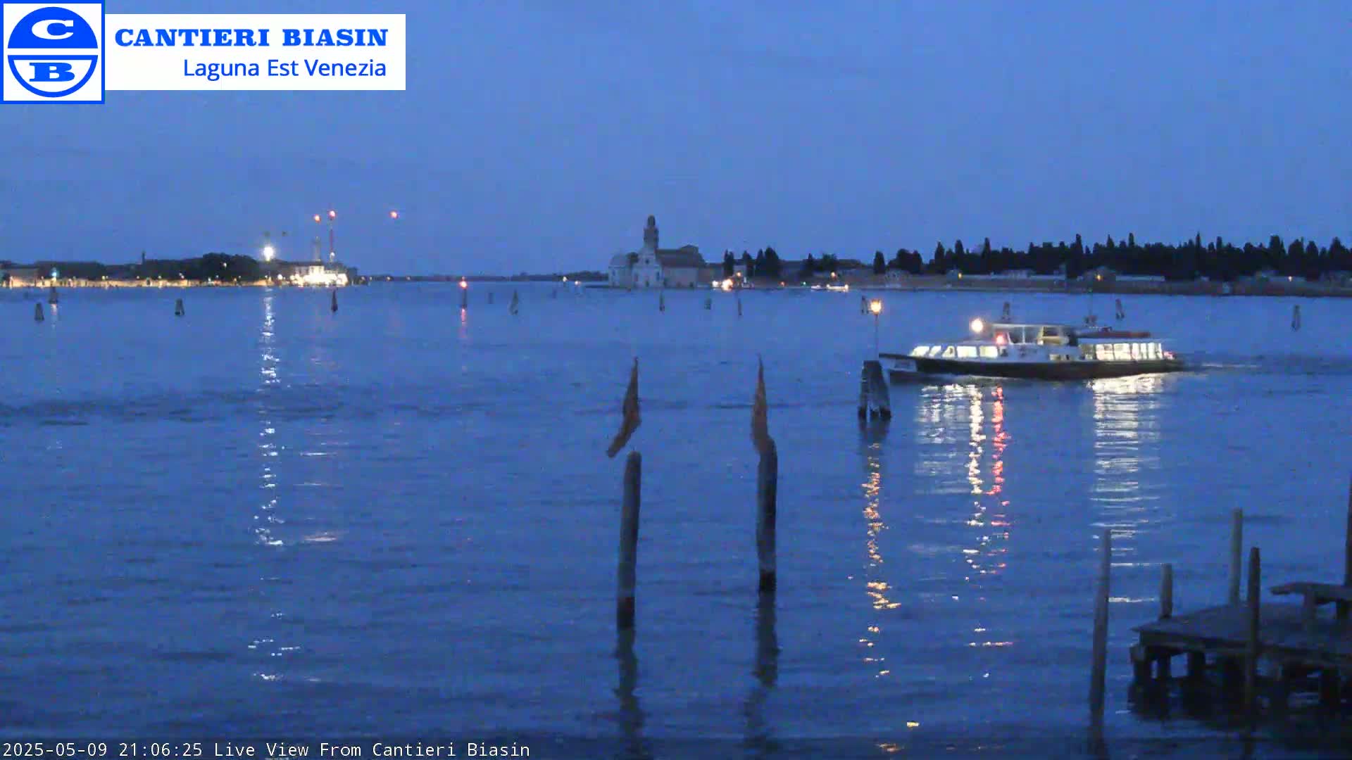 A ferry boat travels across a dark-blue body of water at twilight, passing near a distant island with buildings, under a clear, dusky sky.