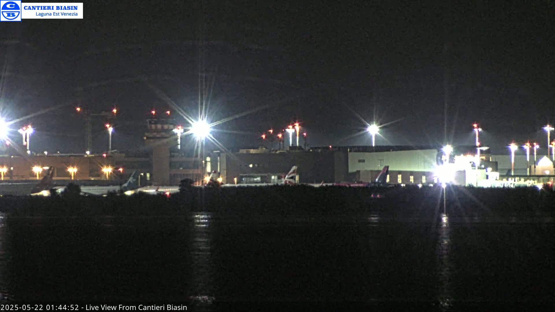 A brightly lit airport at night is seen from across a body of dark water.