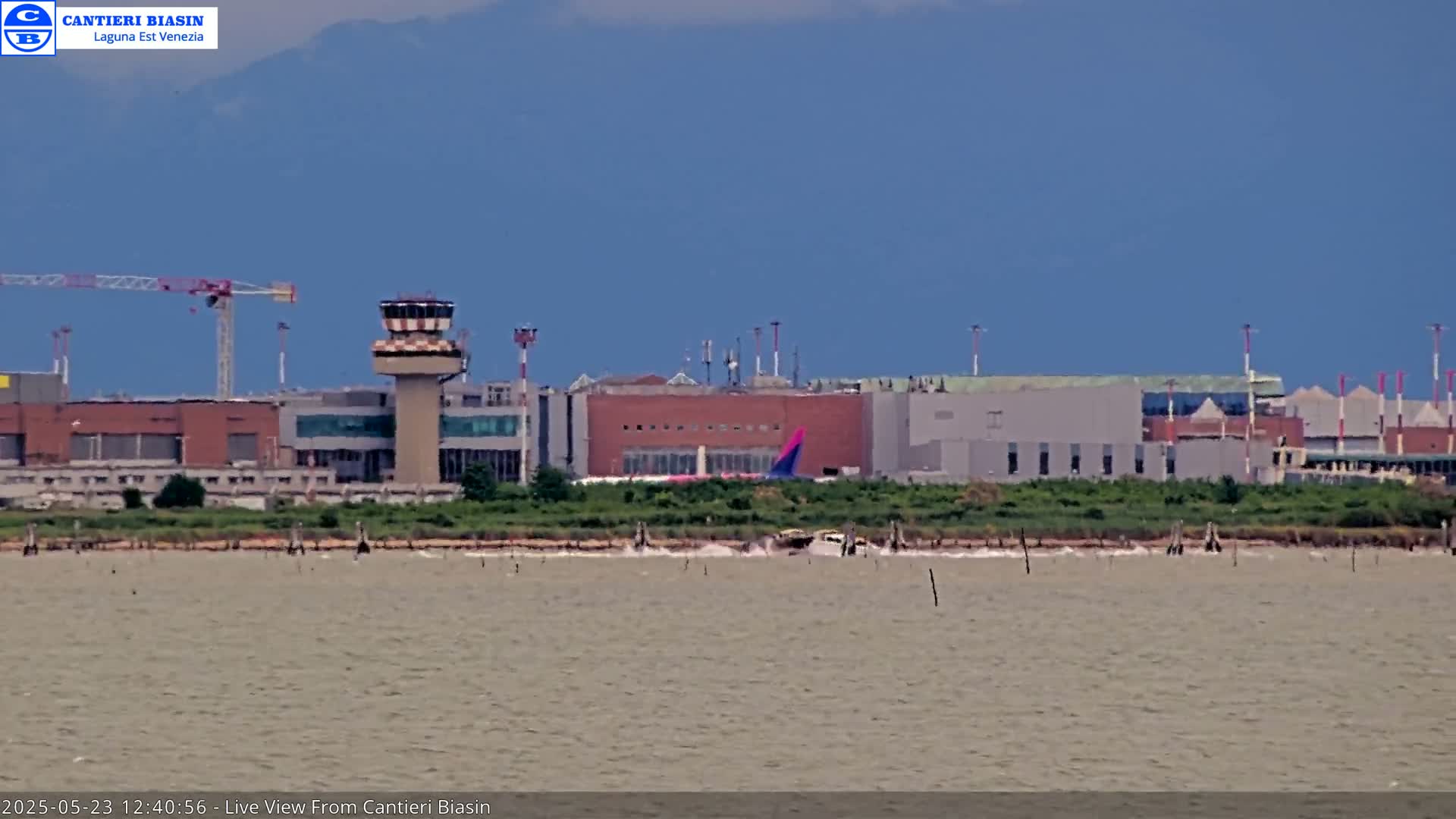 A distant airport with a control tower is visible across a body of calm water under a clear blue sky.