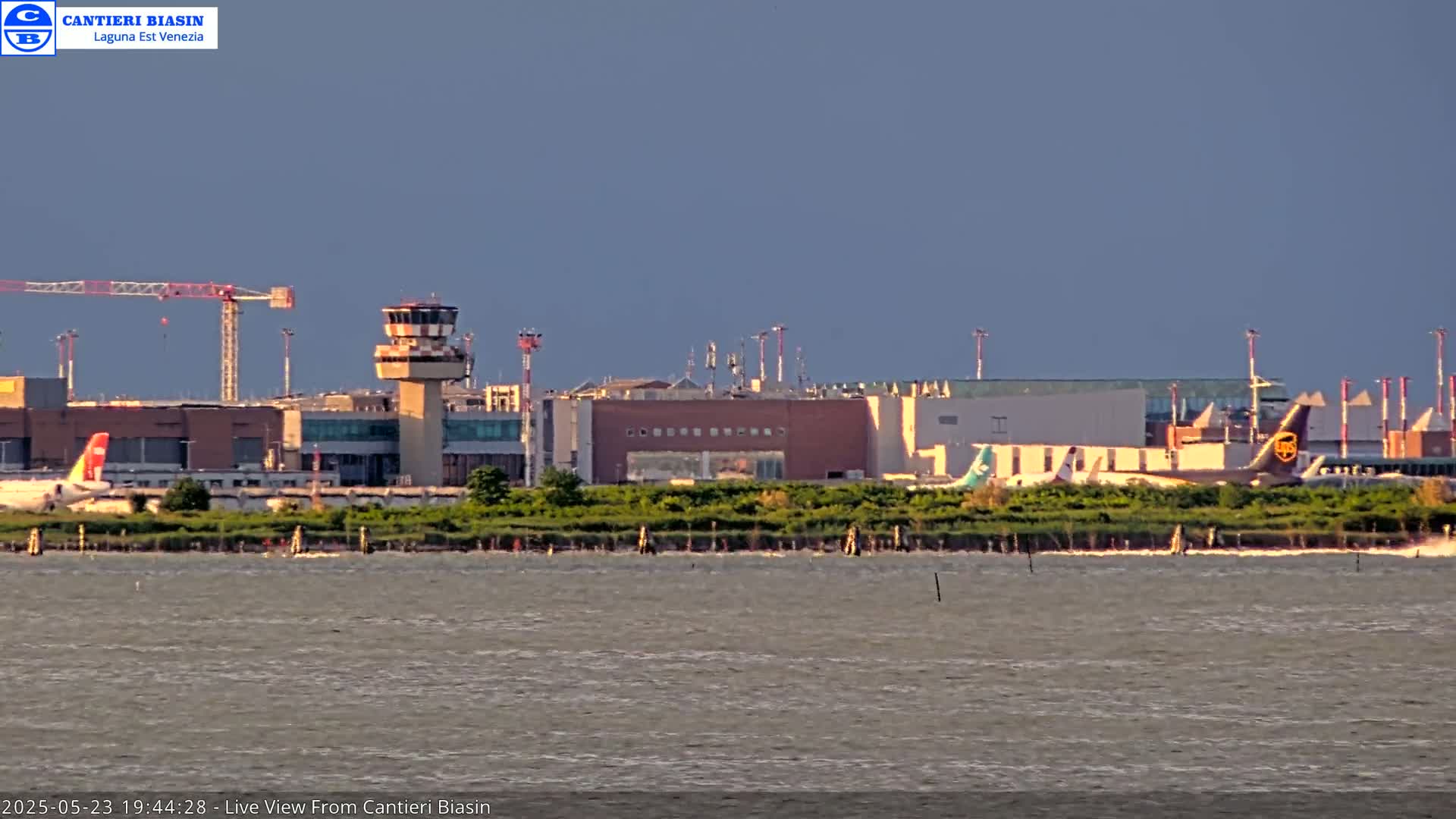 A distant view of an airport with several airplanes on the tarmac, under a partly cloudy sky, across a body of water.