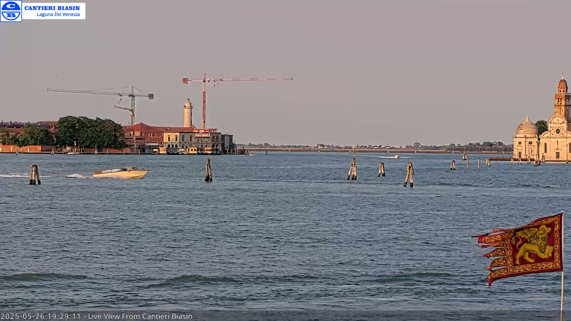 A body of water shows a boat, construction cranes, a lighthouse, buildings, and a church under a hazy sky.