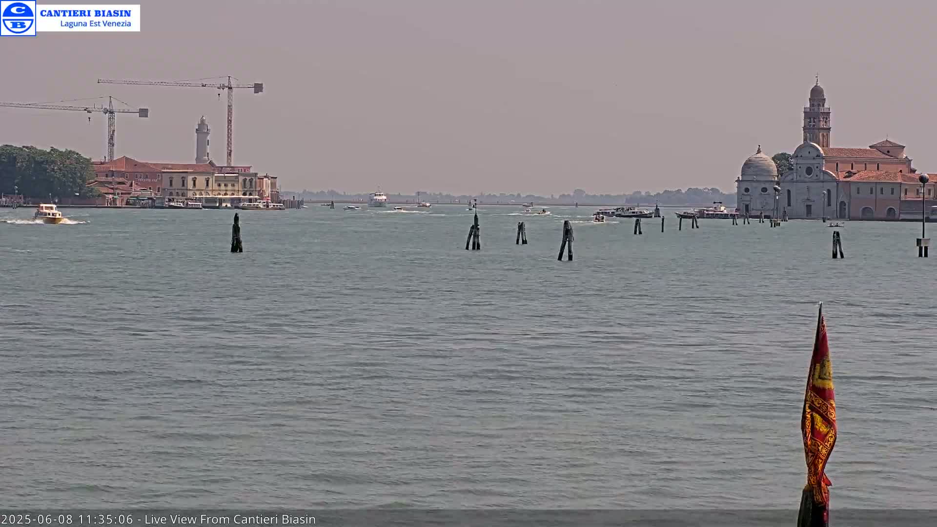 A hazy day shows a calm body of water with several boats and buildings in the distance, including a church with a tall bell tower.