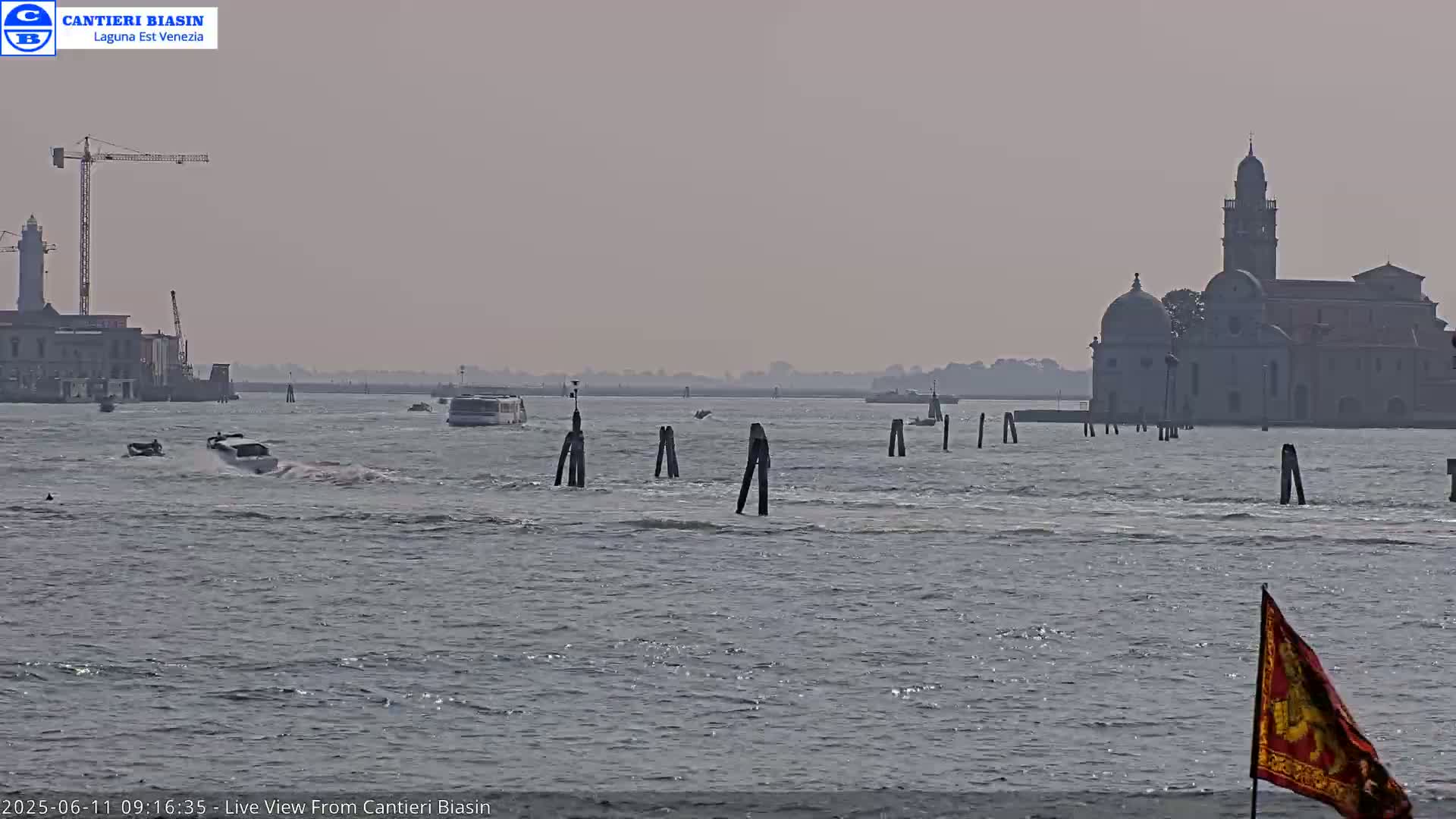 A hazy, light-grey day shows a body of water with several boats, a distant church, and a construction crane on the left.