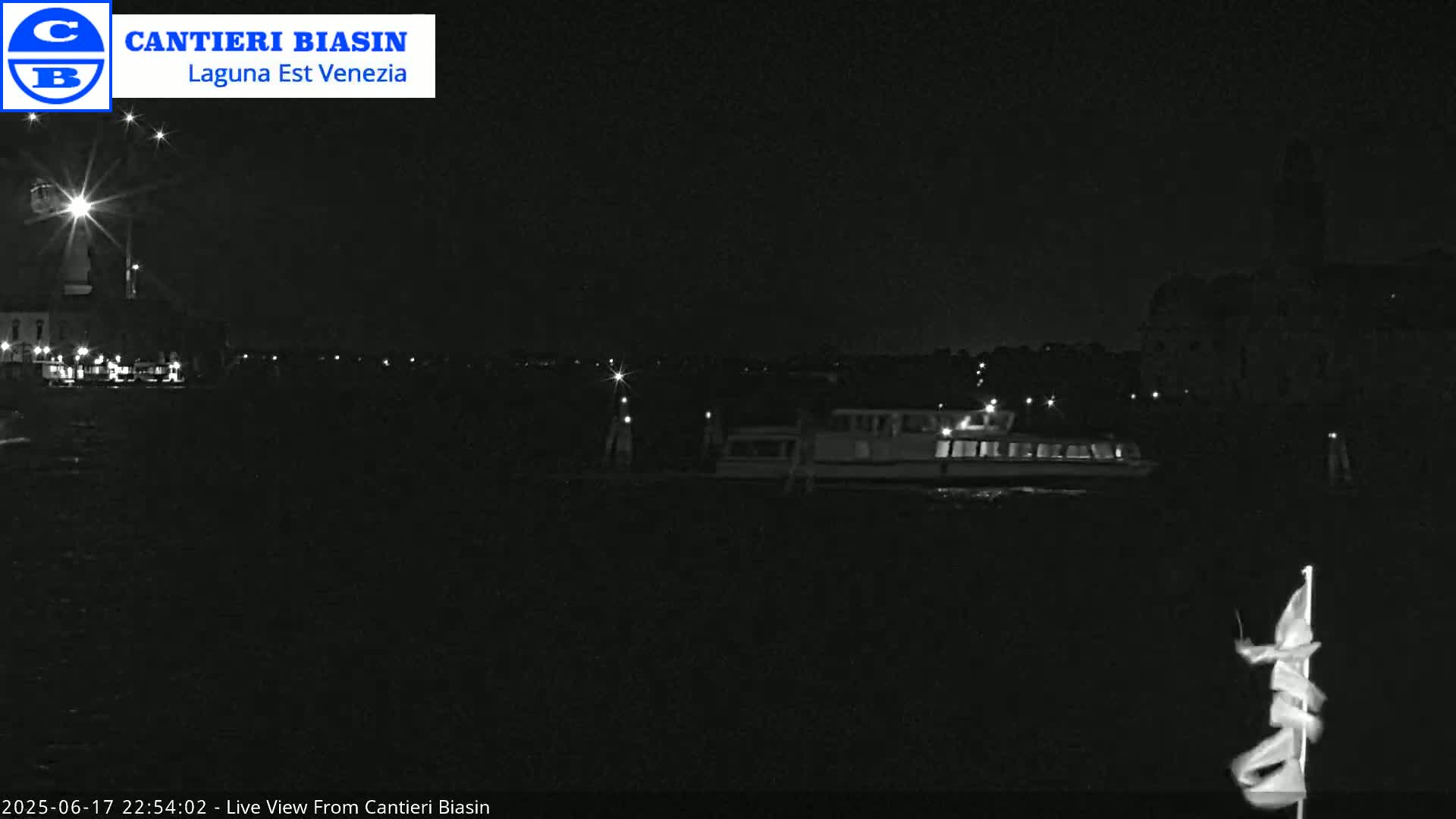 A nighttime, low-light view of a waterway shows a boat and distant lights along the shore.