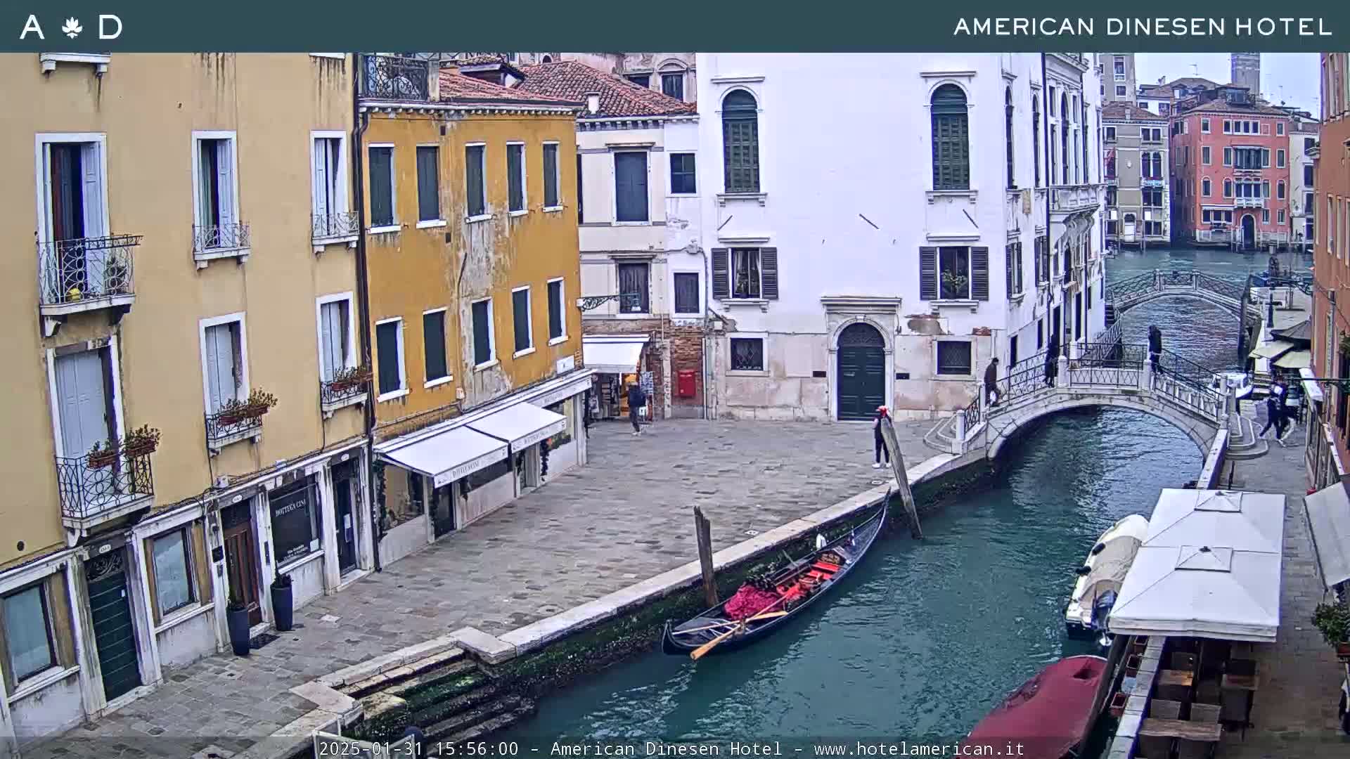 A gondola is moored on a canal beside a stone bridge in Venice, with overcast skies and several buildings lining the waterway.