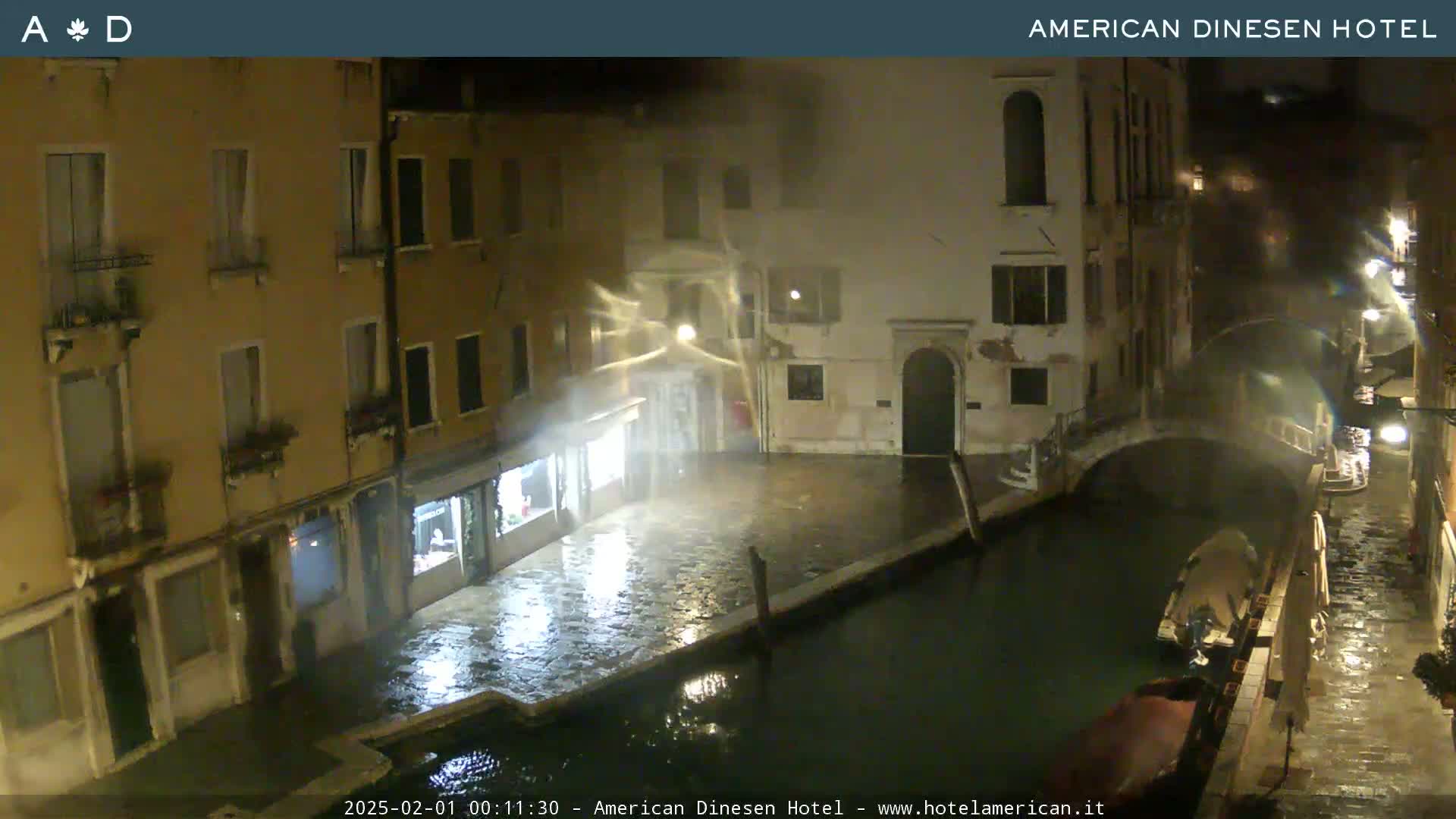 A nighttime view of a canal in Venice, Italy, showing rain and strong winds affecting the waterfront buildings and a gondola.
