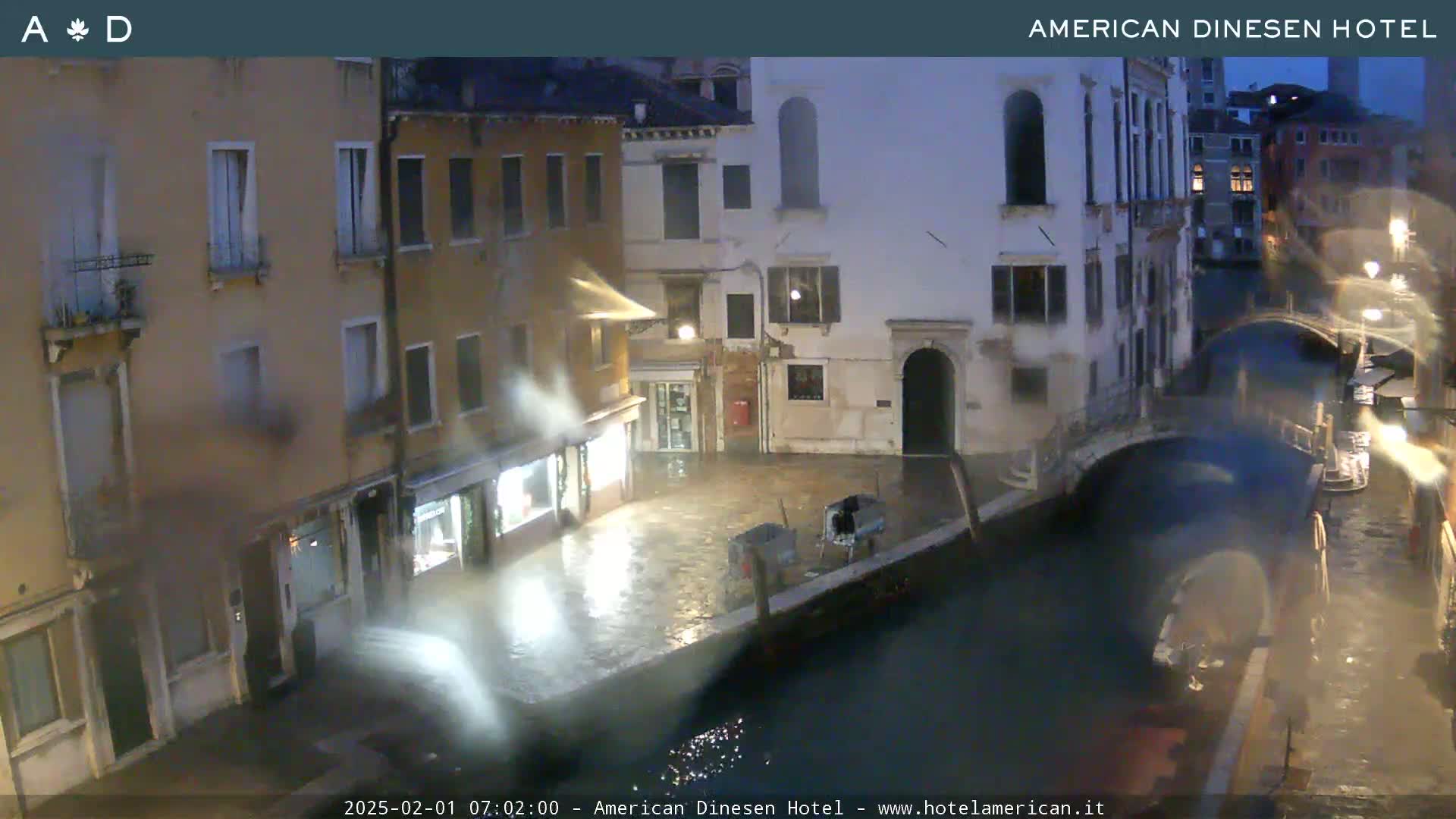 A nighttime view of a canal in Venice, Italy, showing buildings lining the waterway under rainy conditions.