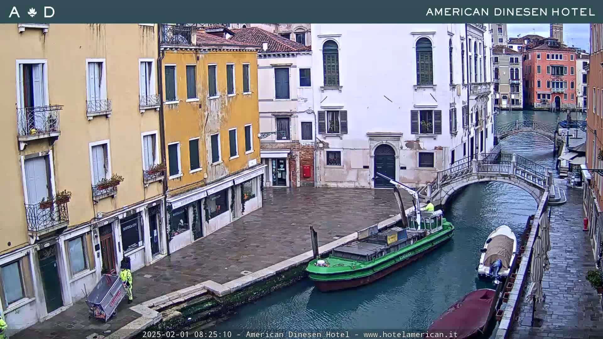 A view of a canal in Venice, Italy, on an overcast day, showing buildings lining the waterway, a small barge, and several smaller boats moored along the canal.