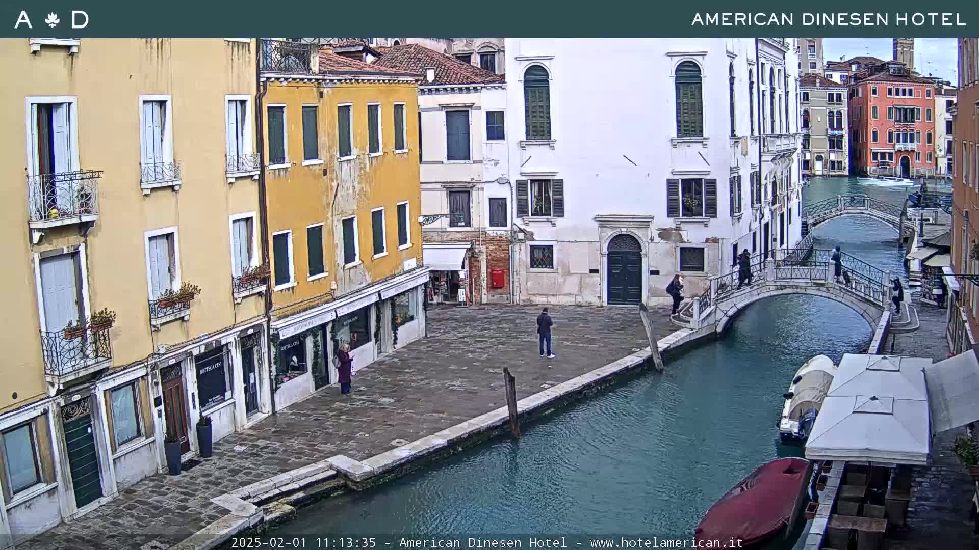 A canal in Venice, Italy, with pedestrians on a footbridge and buildings lining the waterway on a cloudy day.