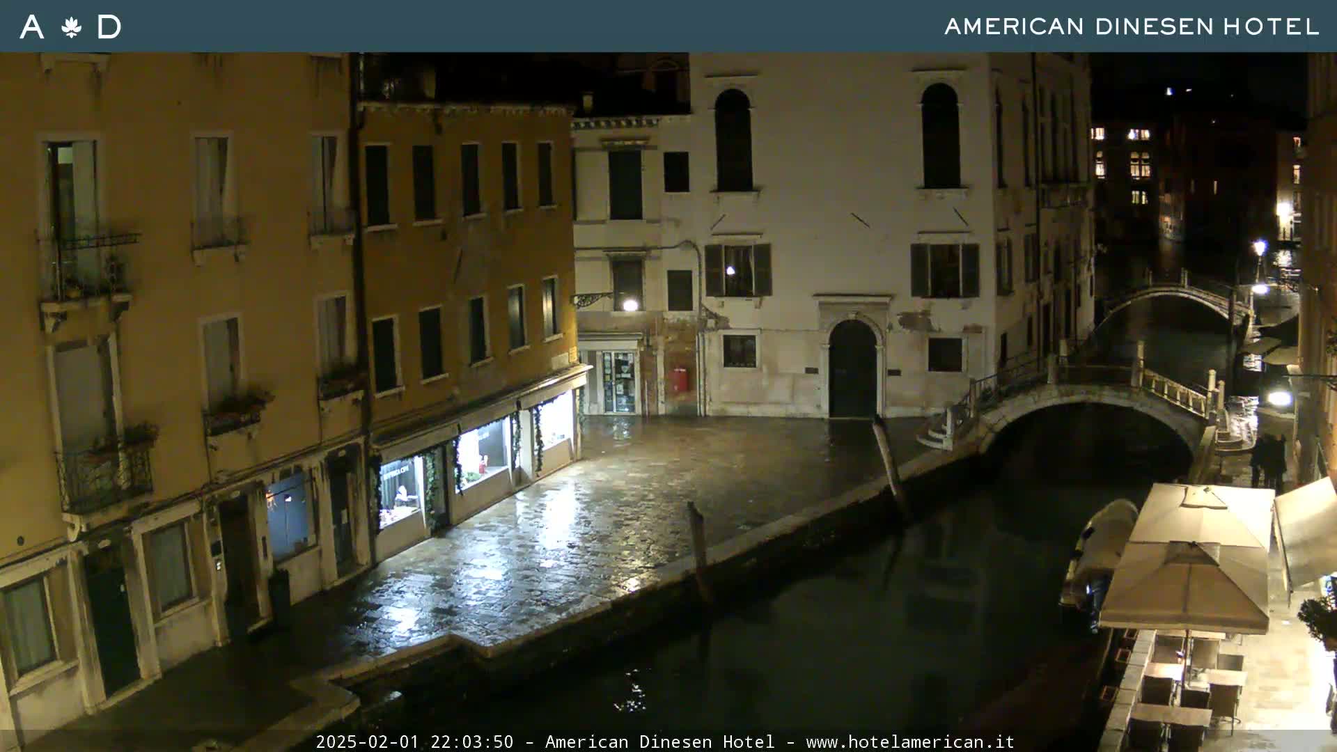 A nighttime view of a canal in Venice, with several buildings lining the waterway, under wet conditions.
