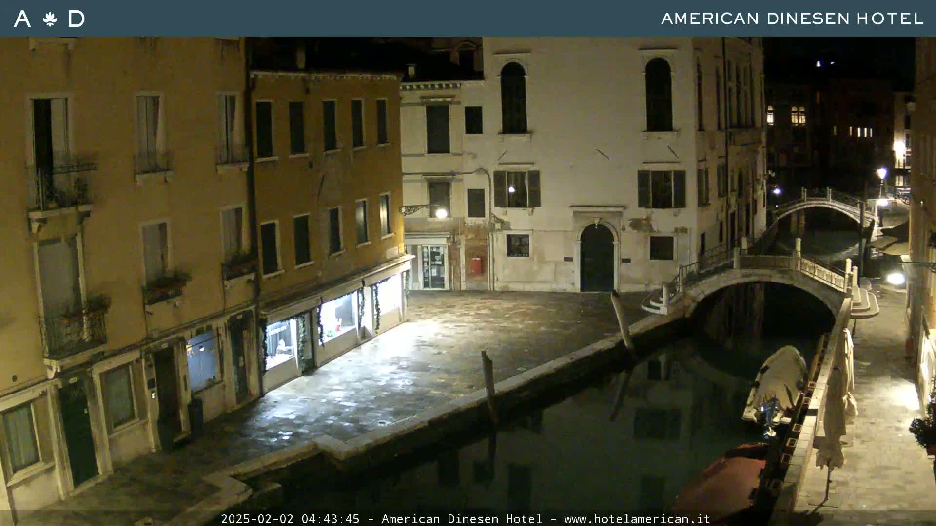 A nighttime view of a canal in Venice, Italy, shows several buildings lining the waterway, with a bridge spanning the canal.