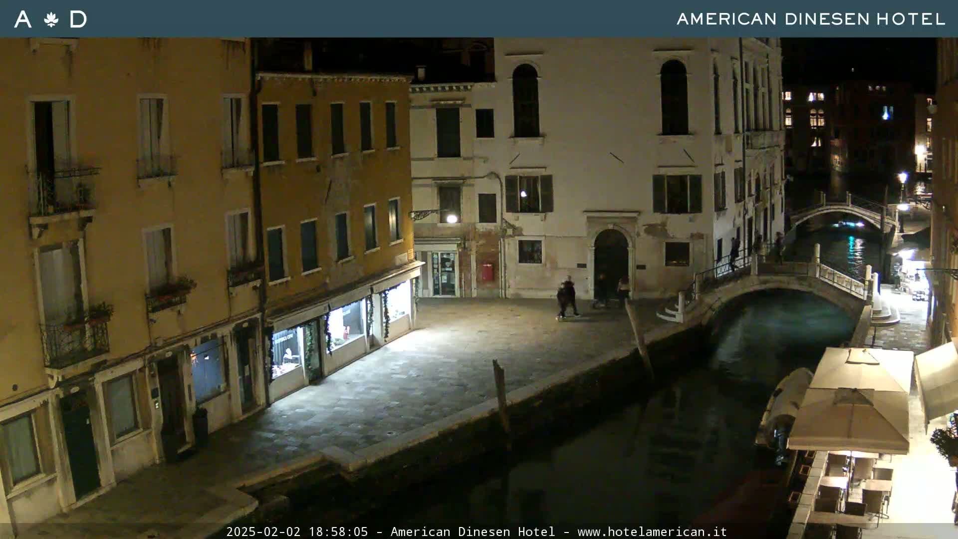 A nighttime view of a canal in Venice, with several buildings lining the waterway and a small bridge crossing it.