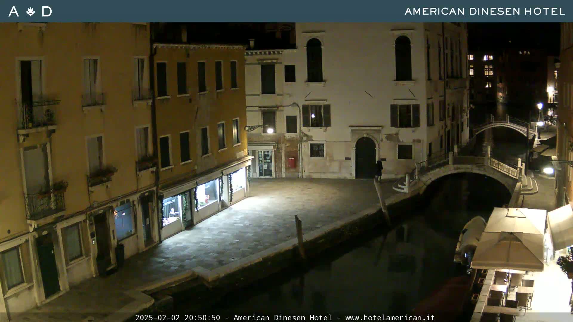 A nighttime view of a canal in Venice, showing several buildings lining the waterway and a small bridge crossing the canal.