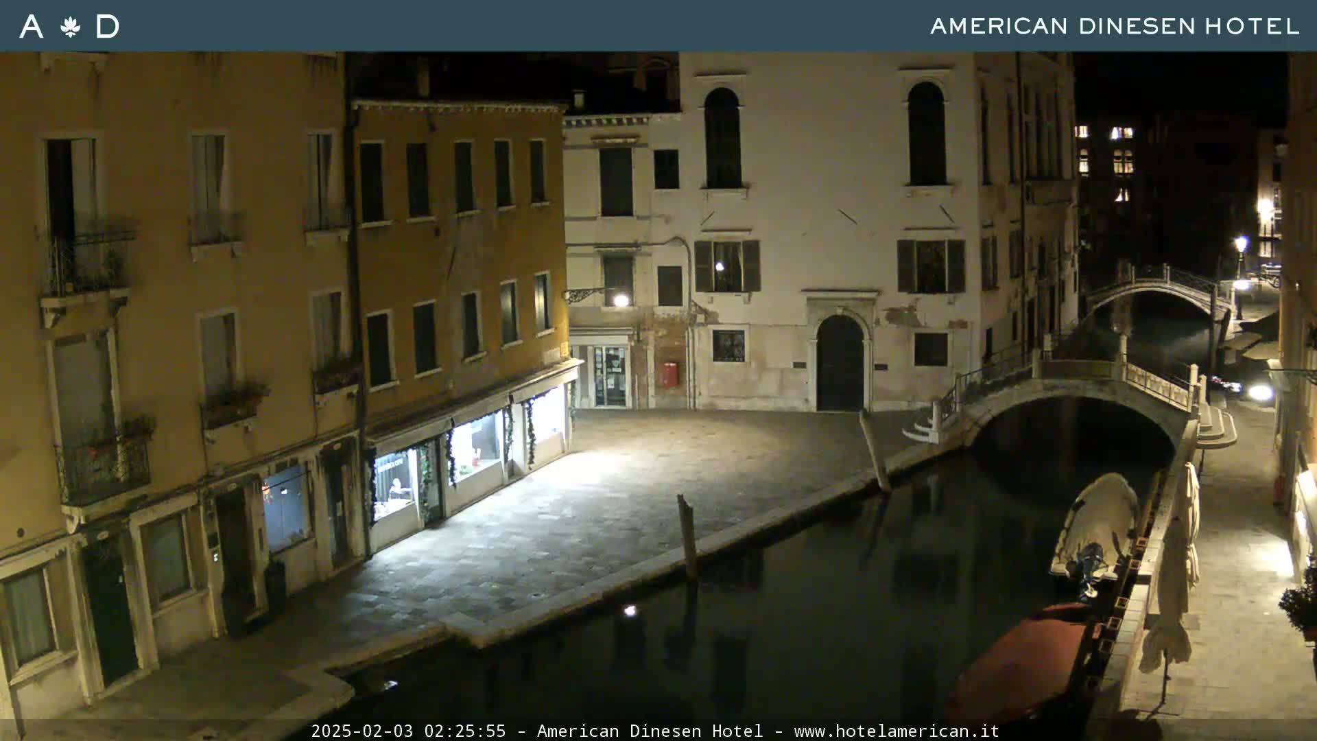 A nighttime view of a canal in Venice, Italy, showing several buildings lining the waterway and a small bridge crossing the canal.