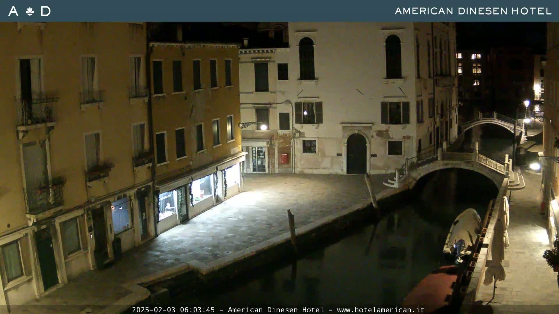 A nighttime view of a canal in Venice, with several buildings lining the waterway and a small bridge spanning the canal.