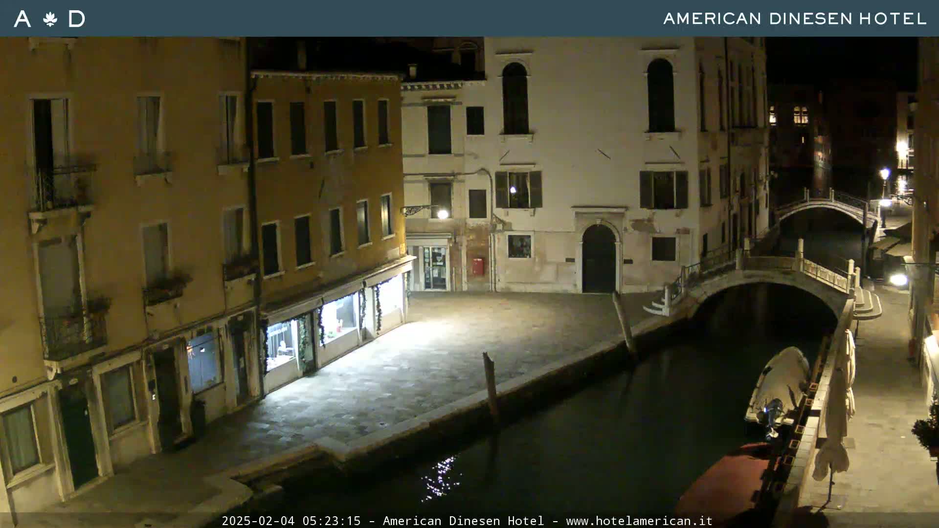 A nighttime view of a canal in Venice, Italy, showing several buildings along the waterway, a bridge, and a small boat moored nearby.