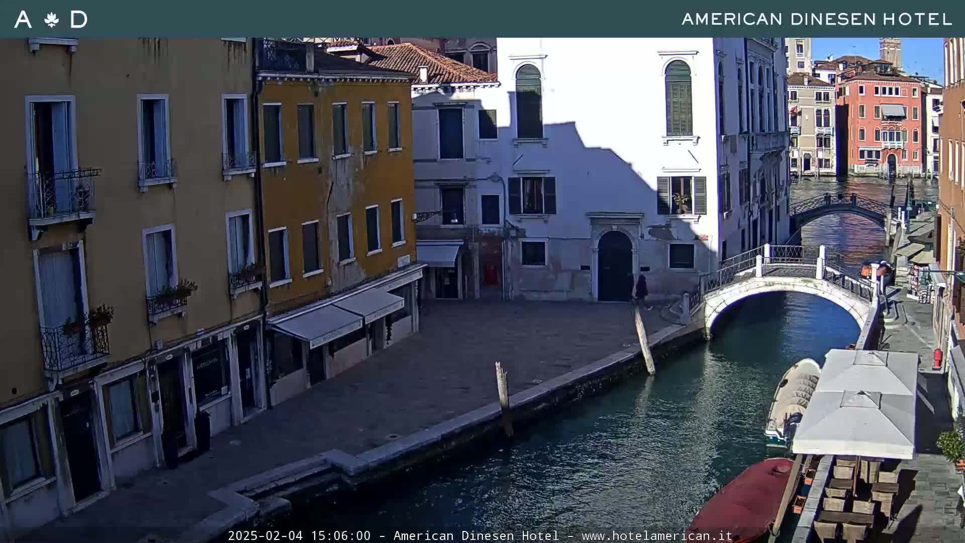 A sunny view of a canal in Venice, Italy, shows colorful buildings lining the waterway, a small bridge, and a boat moored nearby.