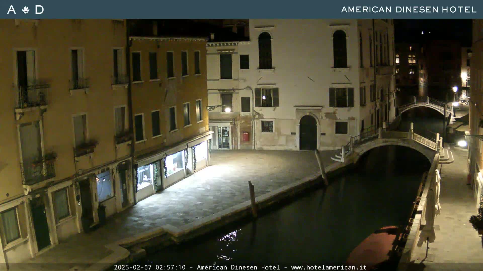A nighttime view of a canal in Venice, with stone buildings lining the waterway and a small bridge spanning the canal.