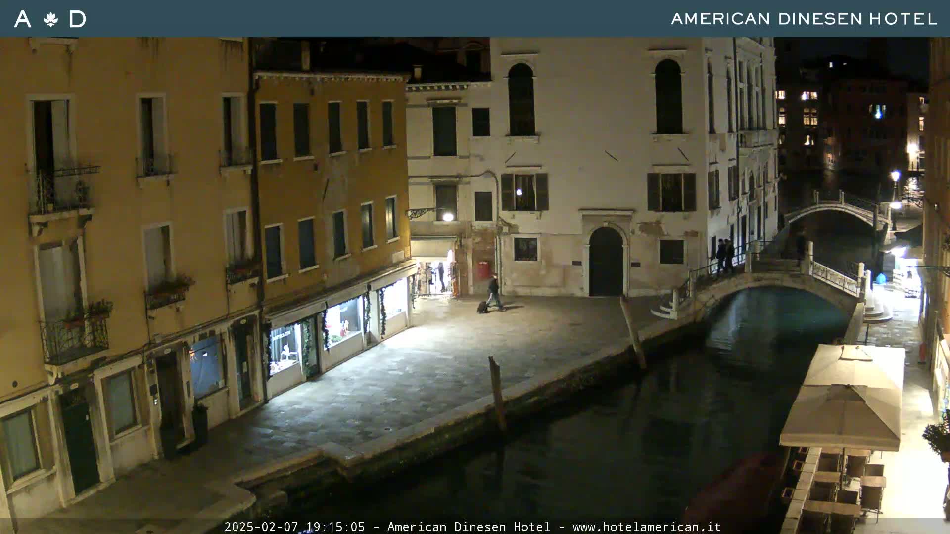 A nighttime view of a canal in Venice, with several buildings lining the waterway and a small bridge crossing it.