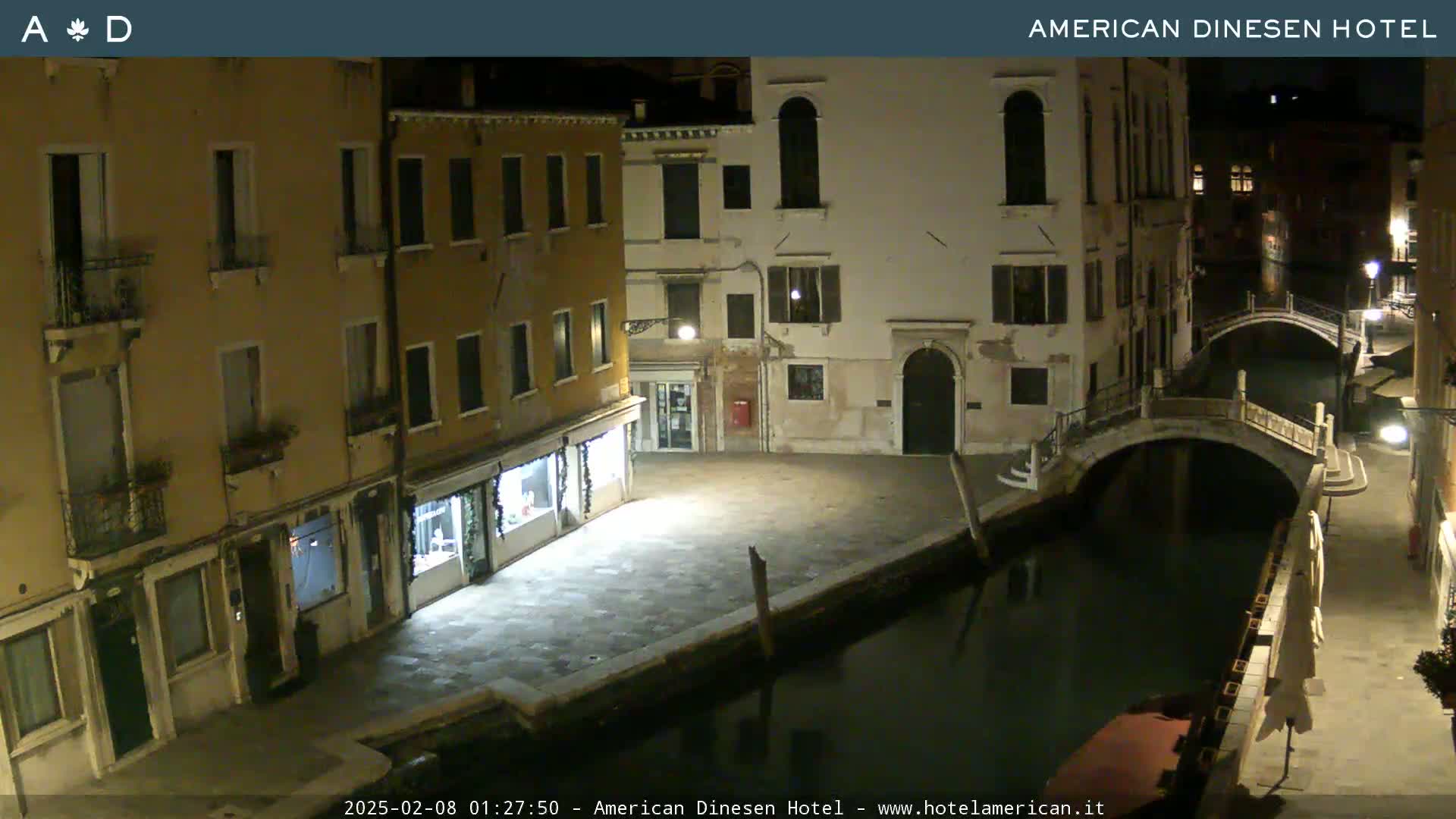 A nighttime view of a canal in Venice, with several buildings lining the waterway and a small bridge spanning the canal.