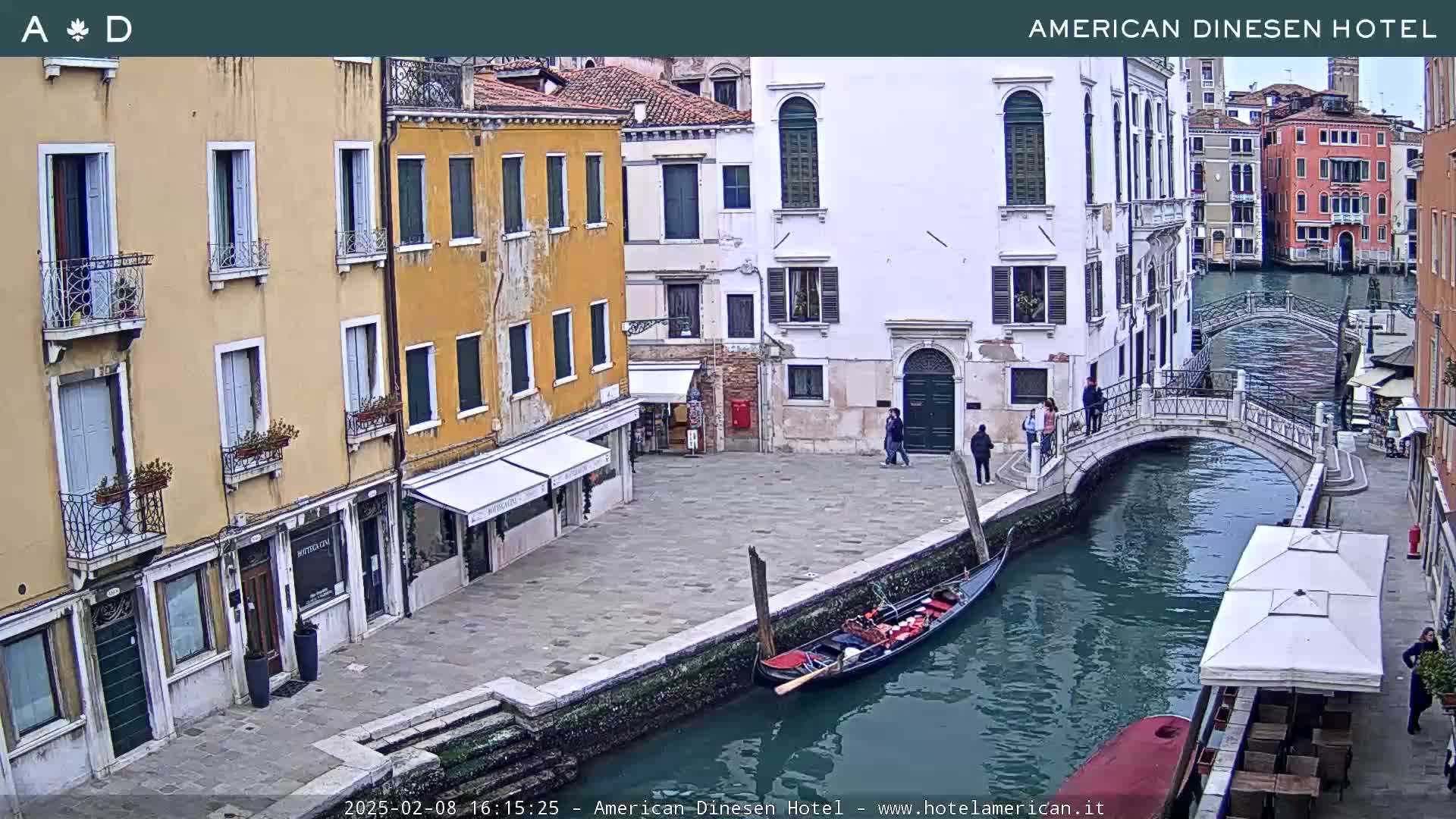 A gondola sits on a canal next to a paved walkway lined with buildings, under an overcast sky.