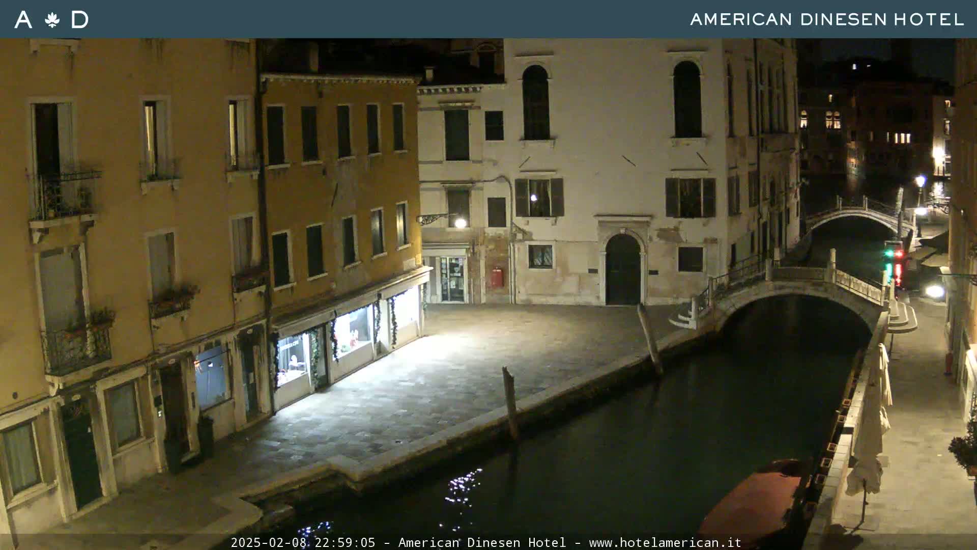 A nighttime view of a canal in Venice, Italy, shows several buildings lining the waterway, with a small bridge spanning the canal.