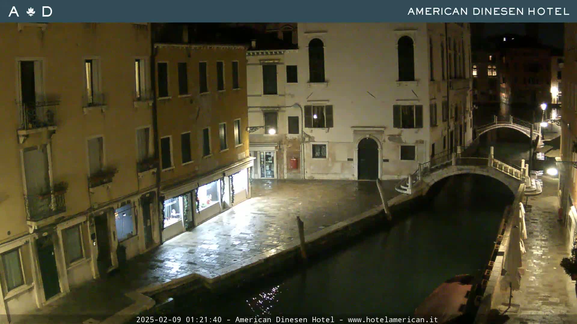 A nighttime view of a canal in Venice, showing stone buildings and bridges under dark, clear skies.