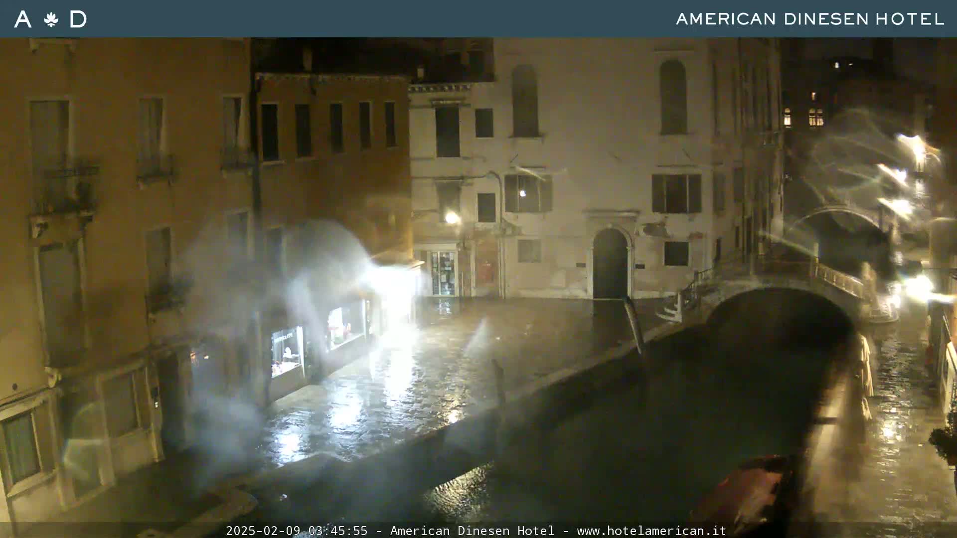 A nighttime view of a canal in Venice, Italy, showing flooded streets and buildings under heavy rain.
