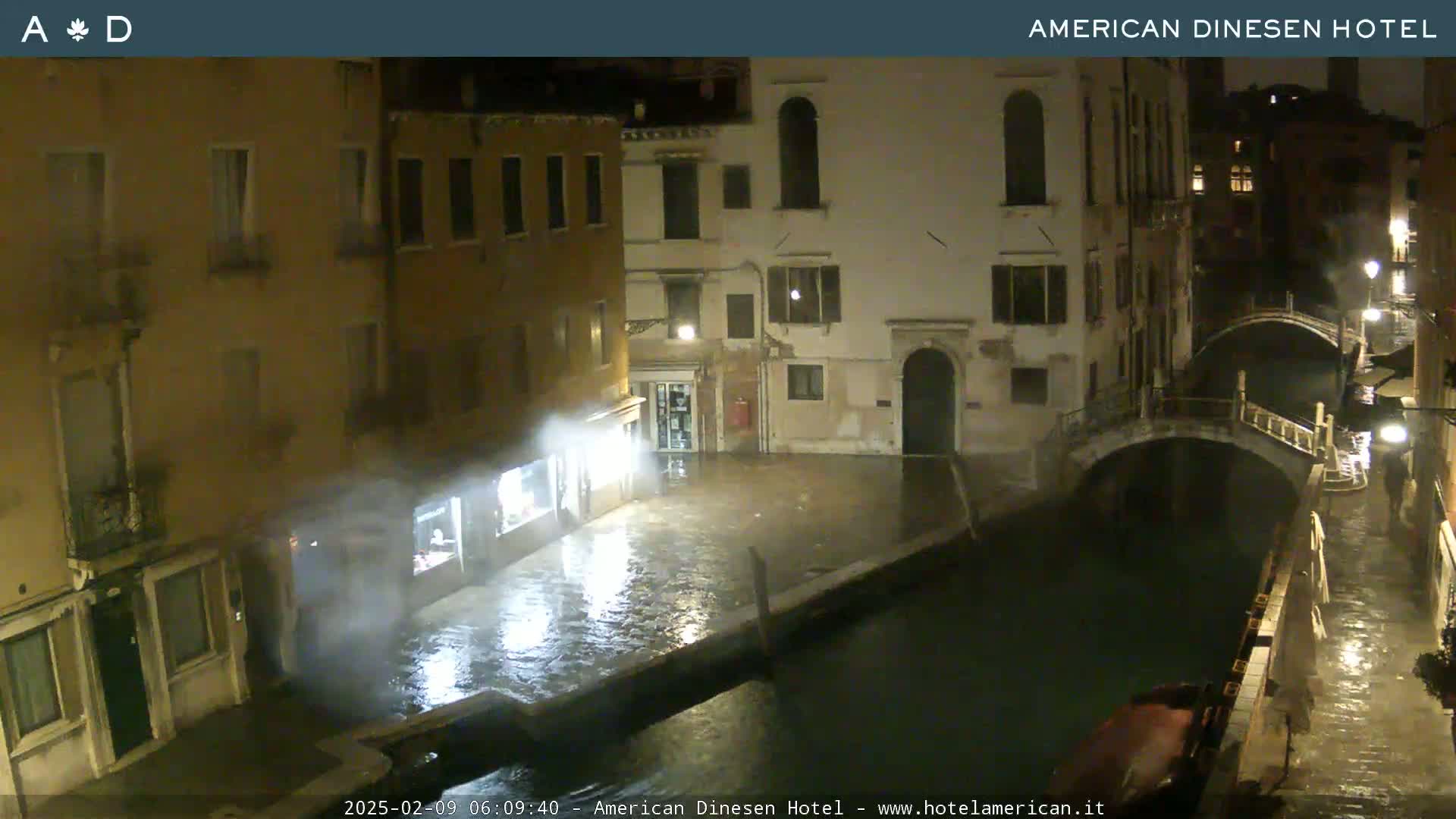 A nighttime view of a flooded canal in Venice, with buildings lining the waterway under rainy conditions.