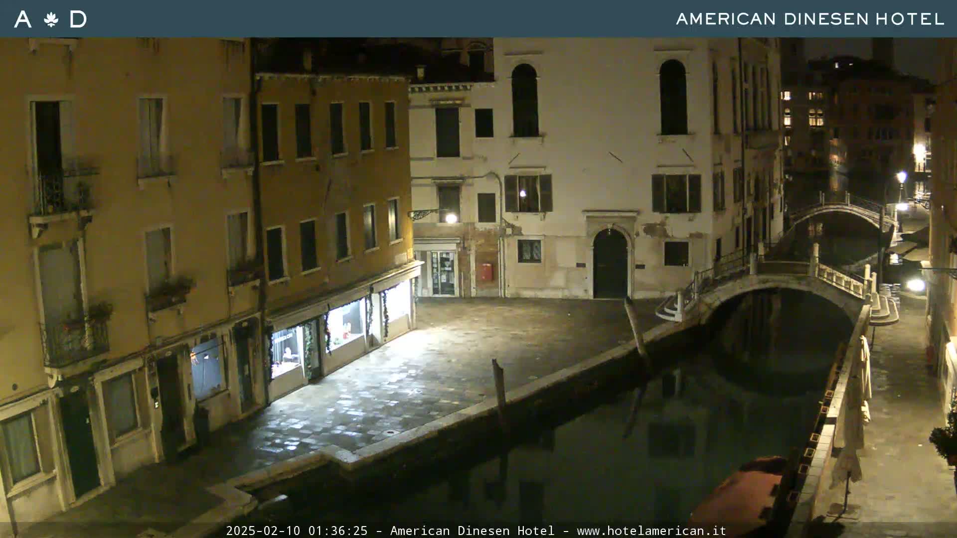 A nighttime view of a canal in Venice, with buildings lining the waterway and a small bridge crossing the canal.
