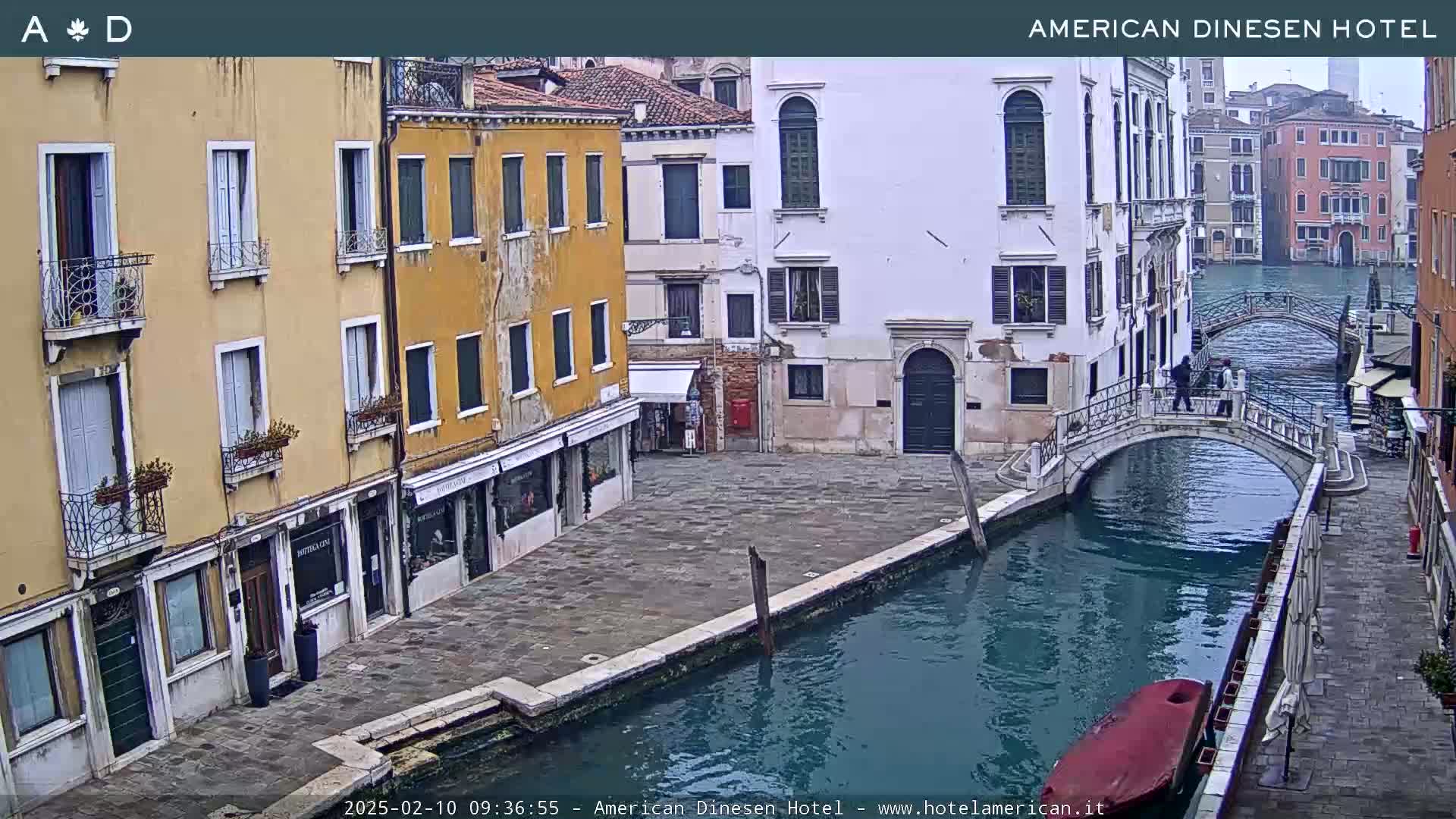 A view of a canal in Venice, Italy, on an overcast day, shows several buildings lining the waterway with a pedestrian bridge crossing the canal.