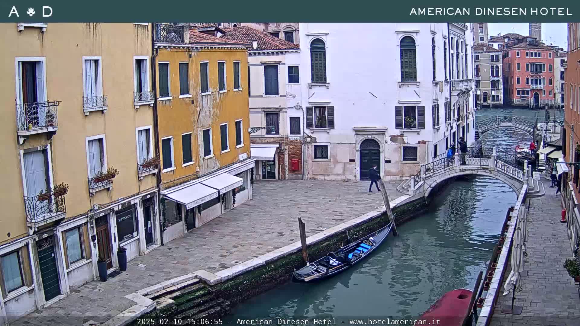 A gondola is moored alongside a canal in Venice, Italy, next to a small stone bridge and several buildings, under an overcast sky.
