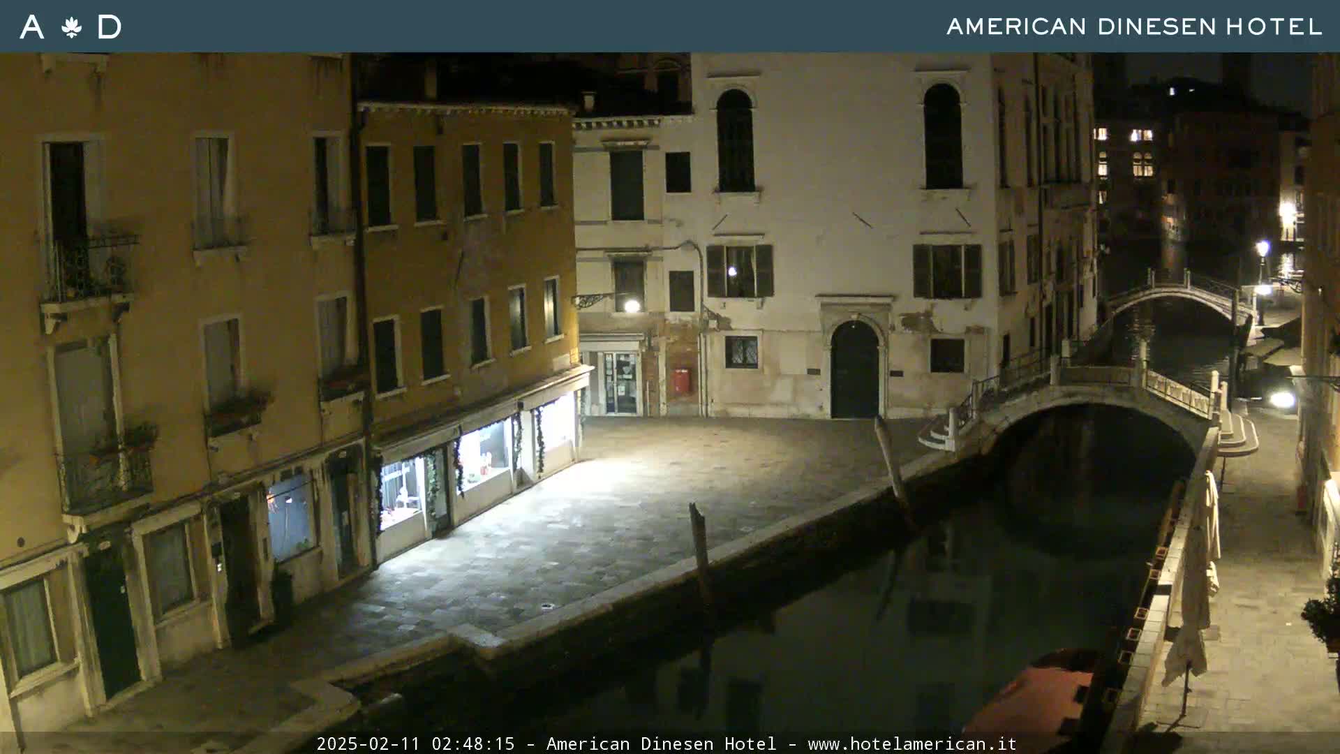 A nighttime view of a canal in Venice, showing several buildings lining the waterway and a small bridge spanning the canal.