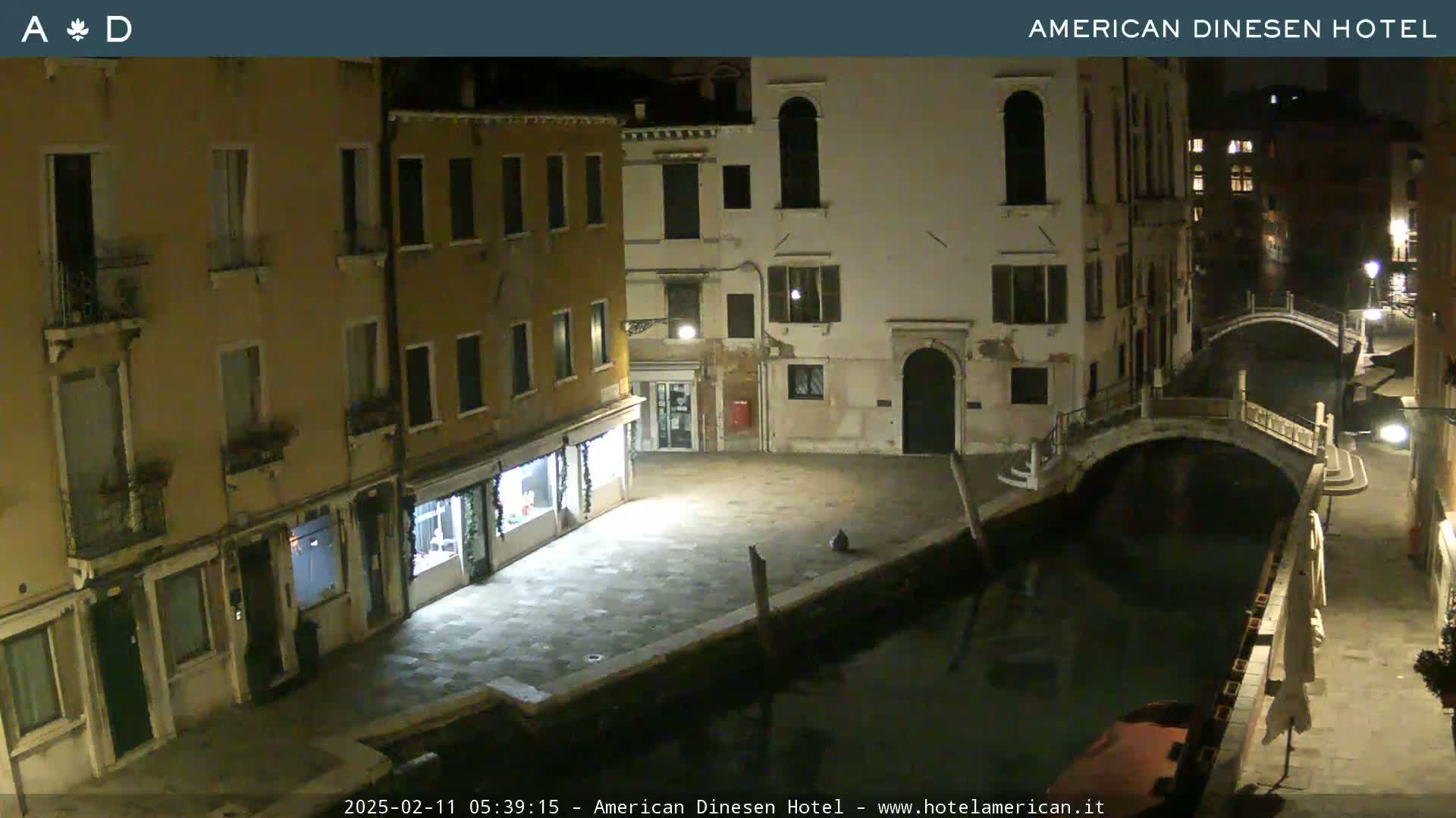 A nighttime view of a canal in Venice, showing buildings lining the waterway and a small bridge spanning the canal.