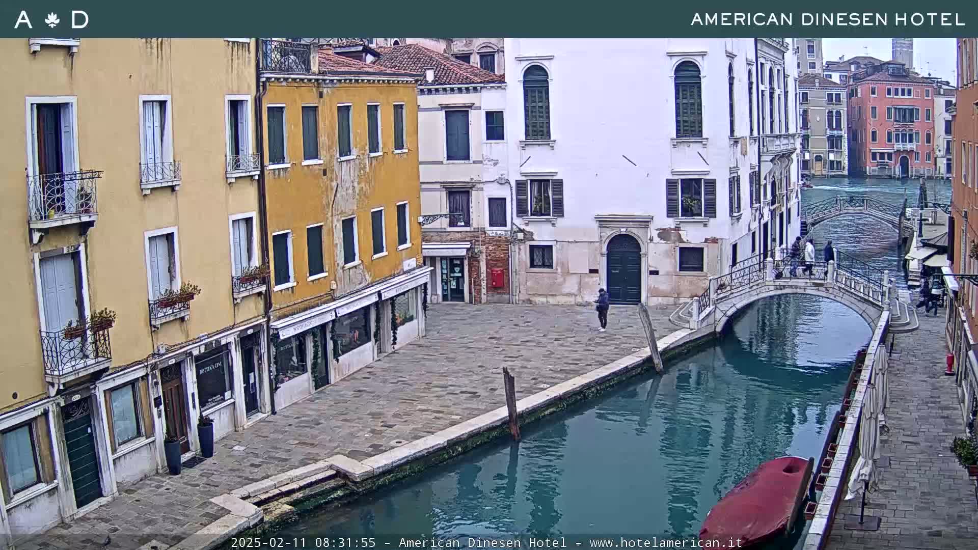 A tranquil canal scene in Venice, featuring colorful buildings lining its banks and a small bridge, under an overcast sky.