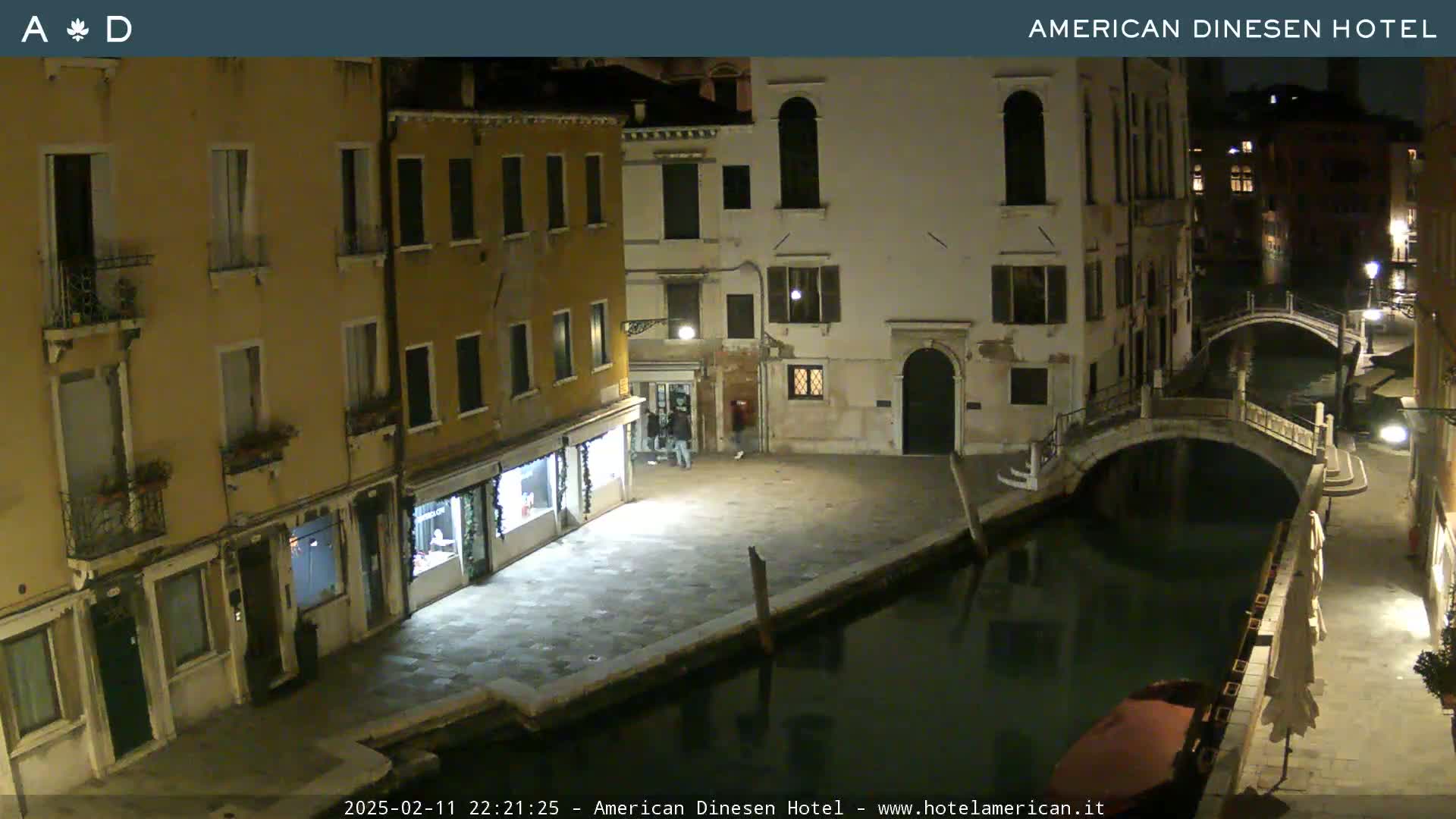 A nighttime view of a canal in Venice, showing stone buildings lining the waterway and a small bridge crossing it.