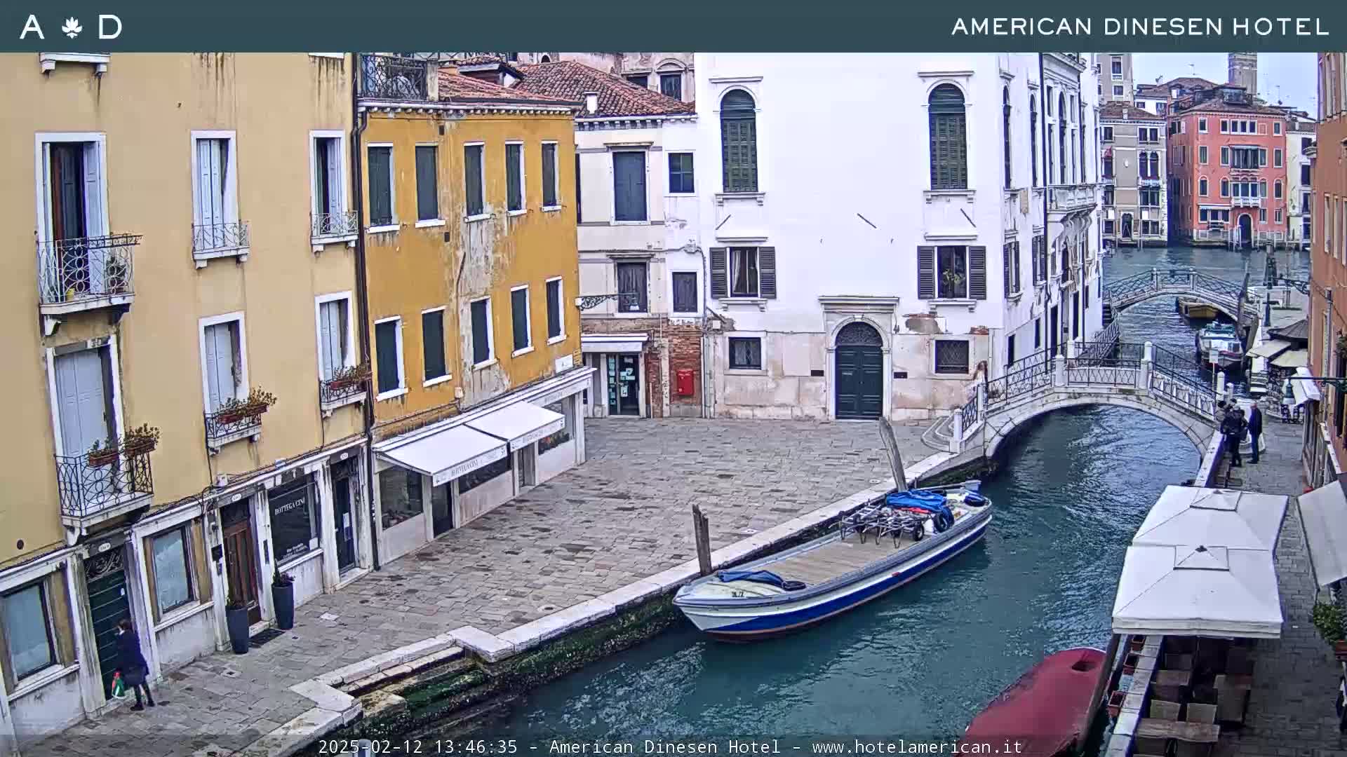 A canal in Venice, Italy, shows several buildings along its banks, a small bridge, a boat with bikes on it, and an overcast sky.
