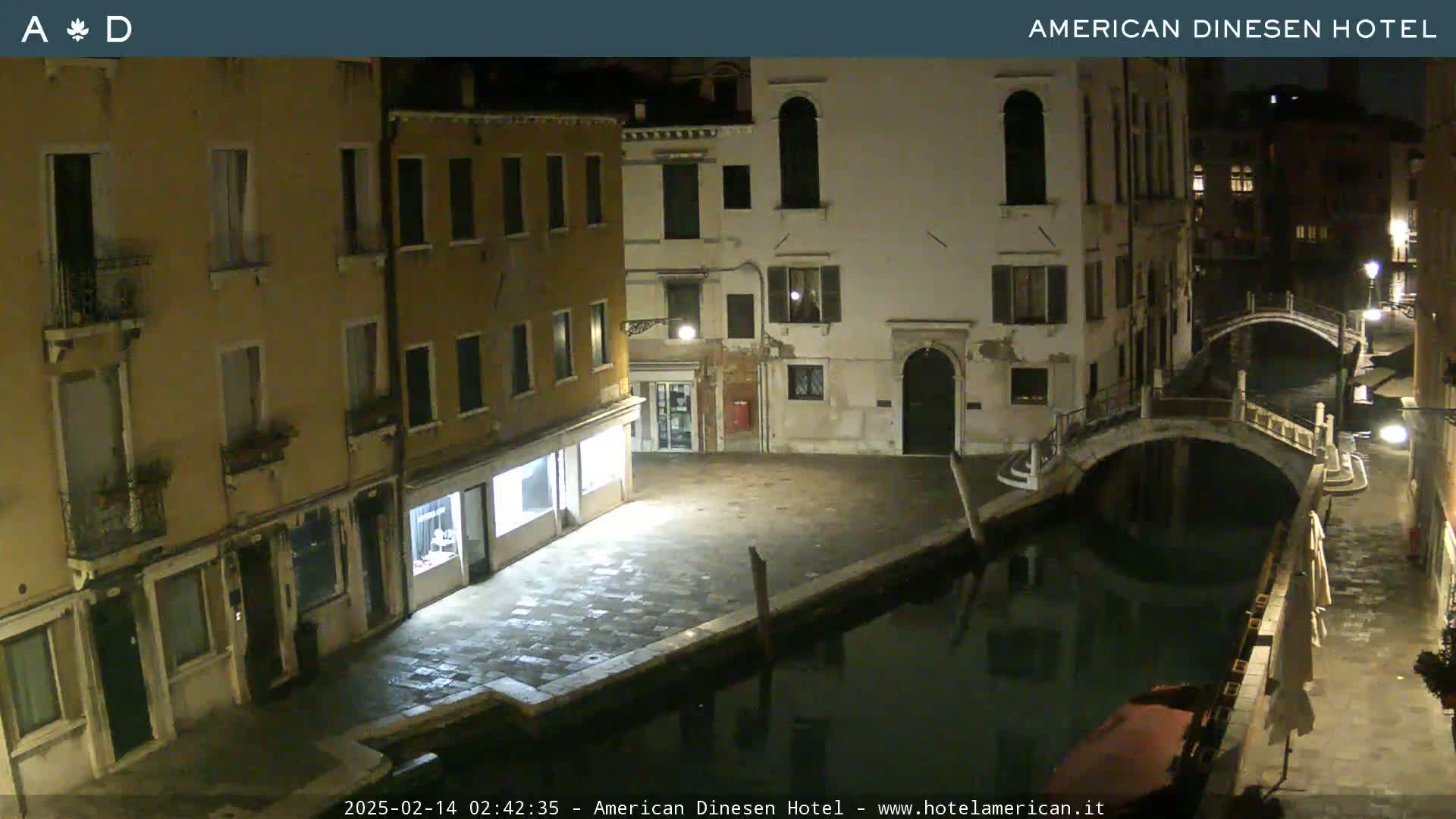 A nighttime view of a canal in Venice, showing stone buildings and a small bridge, under a clear sky.