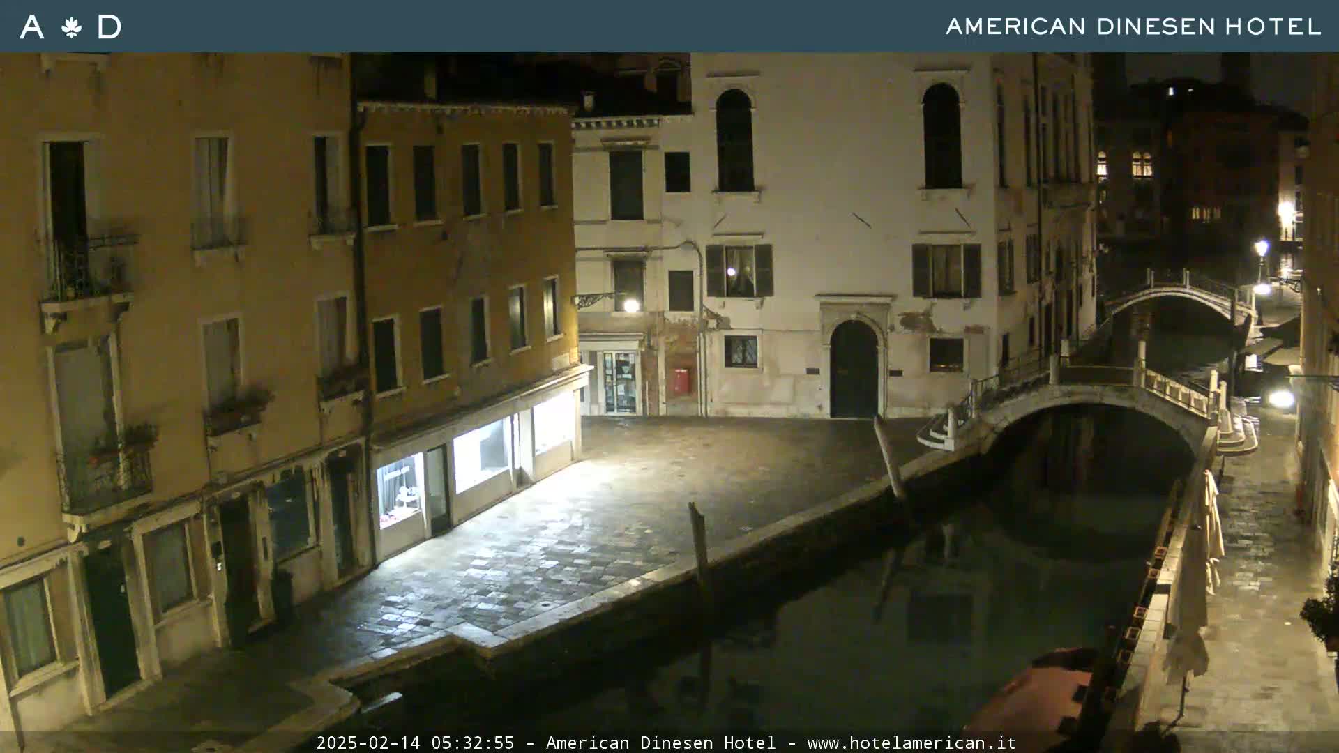 A nighttime view of a canal in Venice, showing several buildings along its banks, one of which has a bridge crossing it.