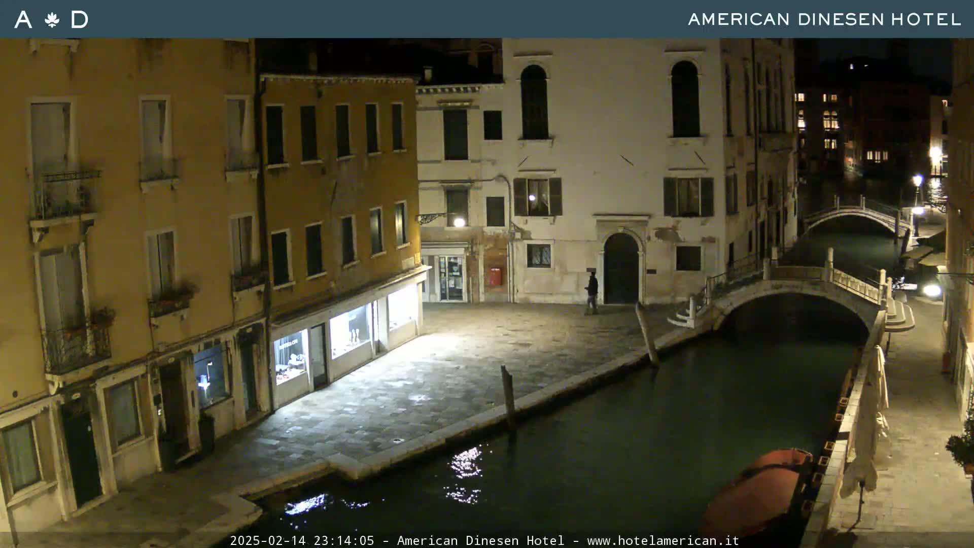 A nighttime view of a canal in Venice, Italy, with buildings lining the waterway and a small boat moored alongside a bridge.