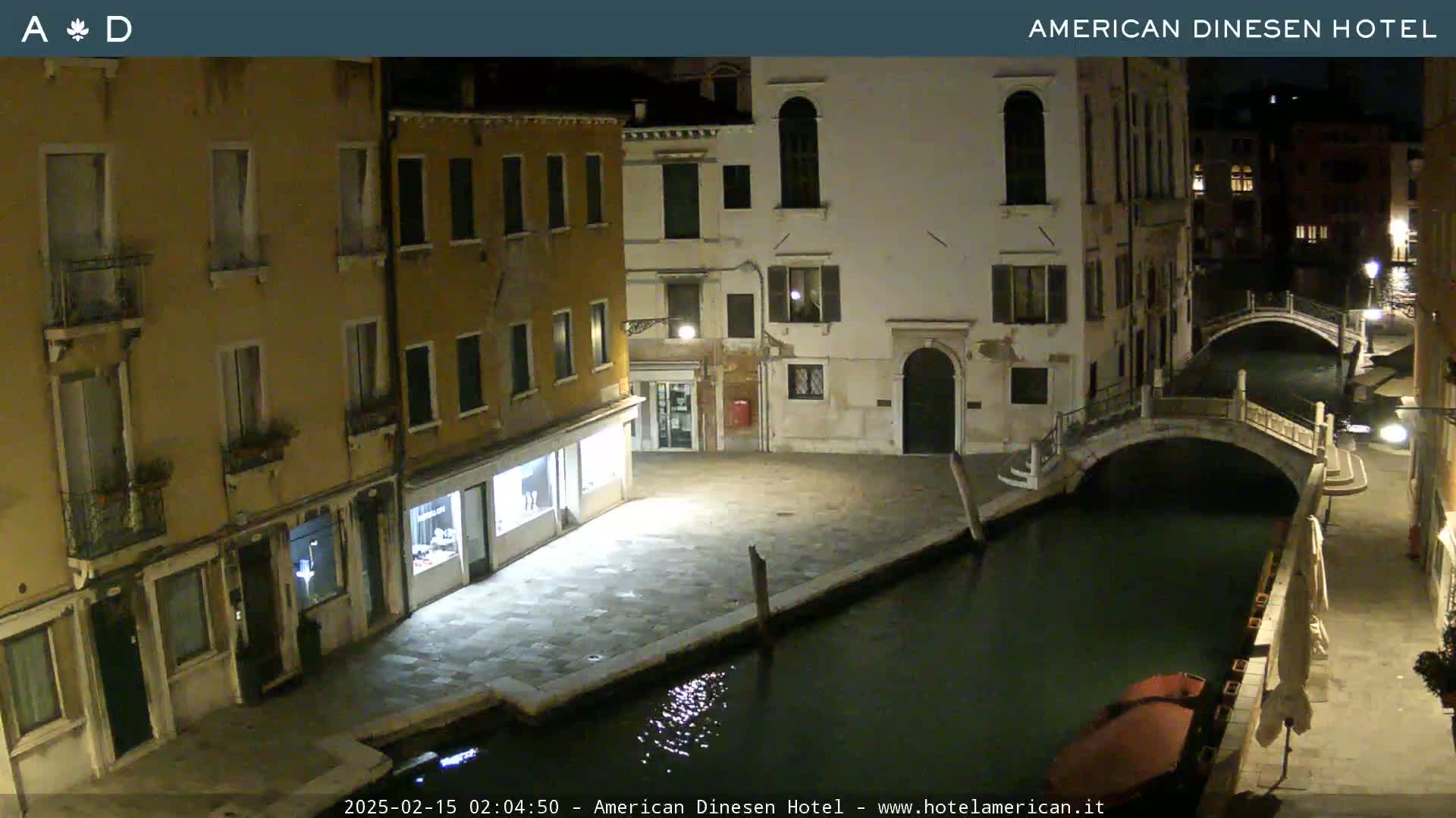 A nighttime view of a canal in Venice, showing buildings lining the waterway and a small bridge spanning the canal.