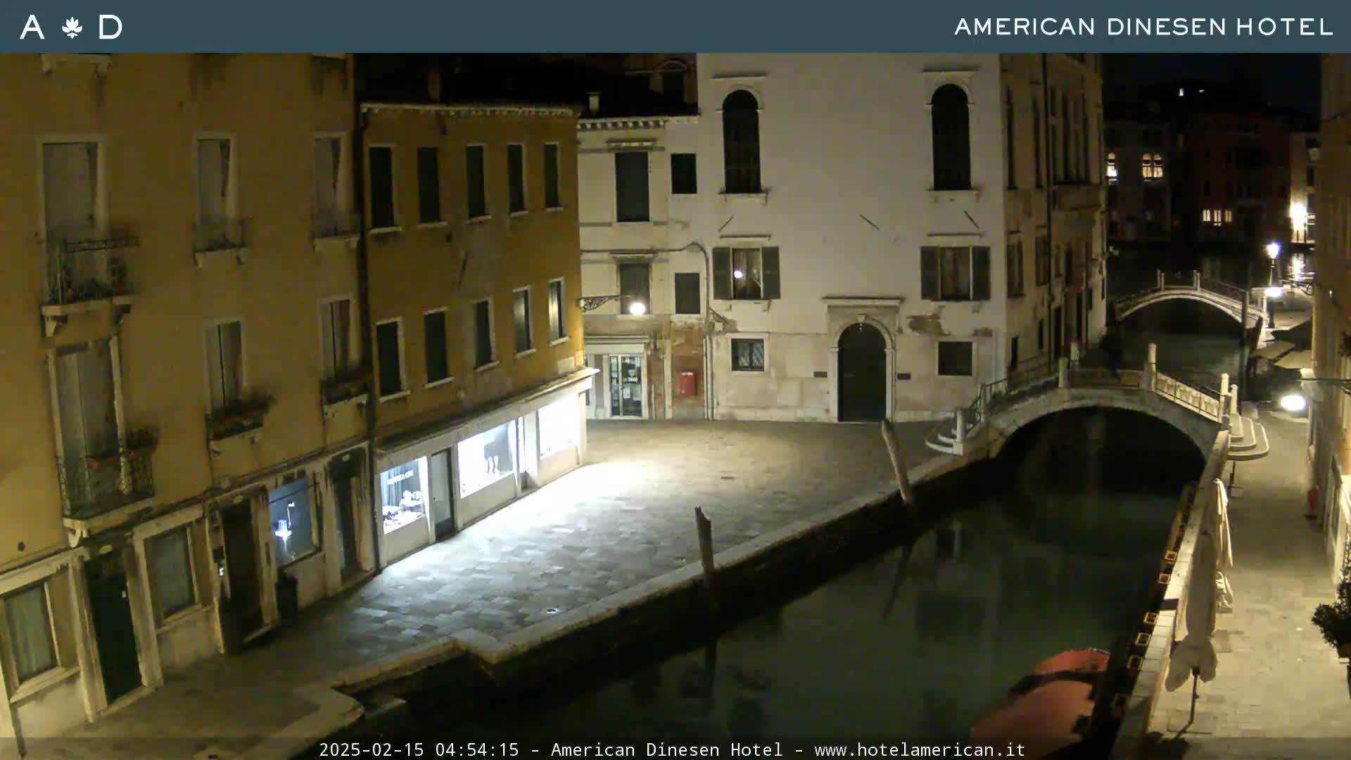 A nighttime view of a canal in Venice, with stone buildings lining the waterway and a small bridge spanning the canal.