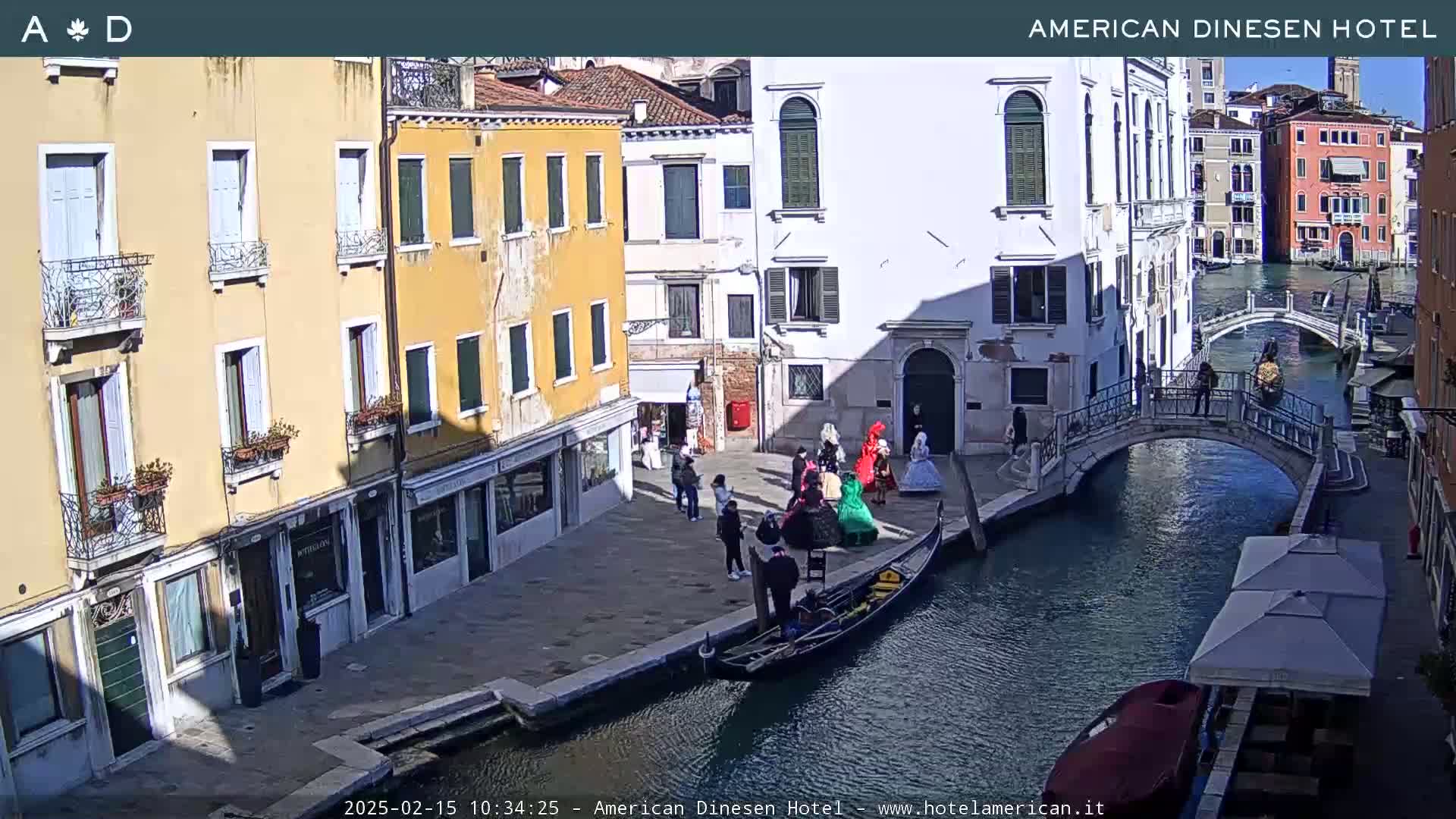 A sunny Venetian canal scene shows a gondola, several people in period costumes, and buildings lining the waterway and a small bridge.