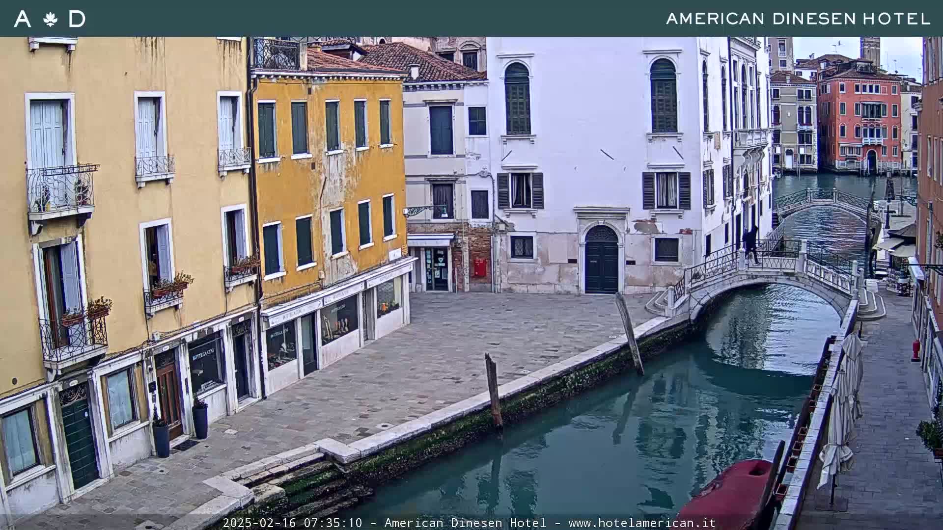 A view of a canal in Venice, Italy, showing several buildings along its banks and a small bridge crossing the waterway under an overcast sky.