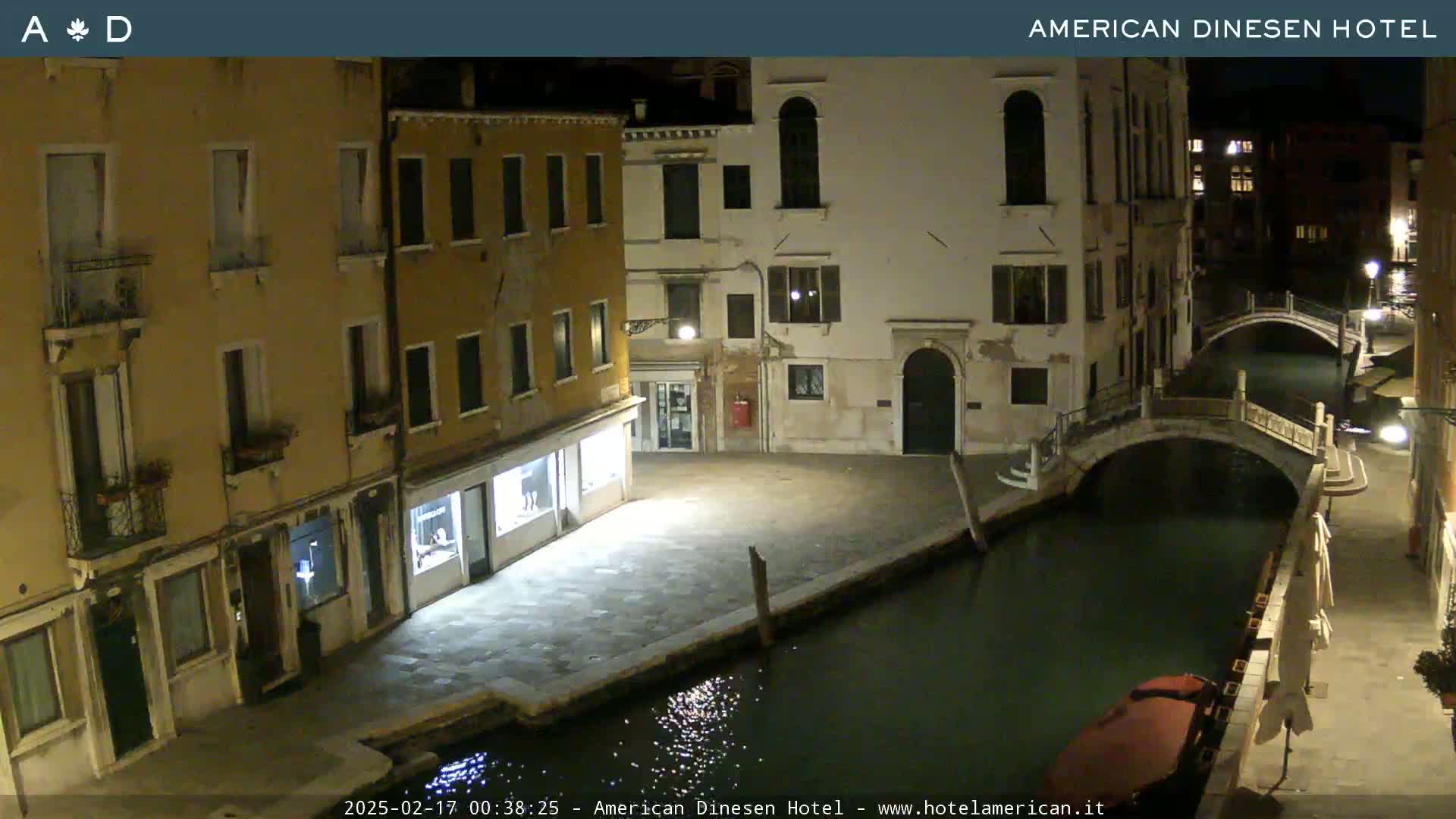 A nighttime view of a canal in Venice, with stone buildings lining the waterway and a small boat moored alongside.